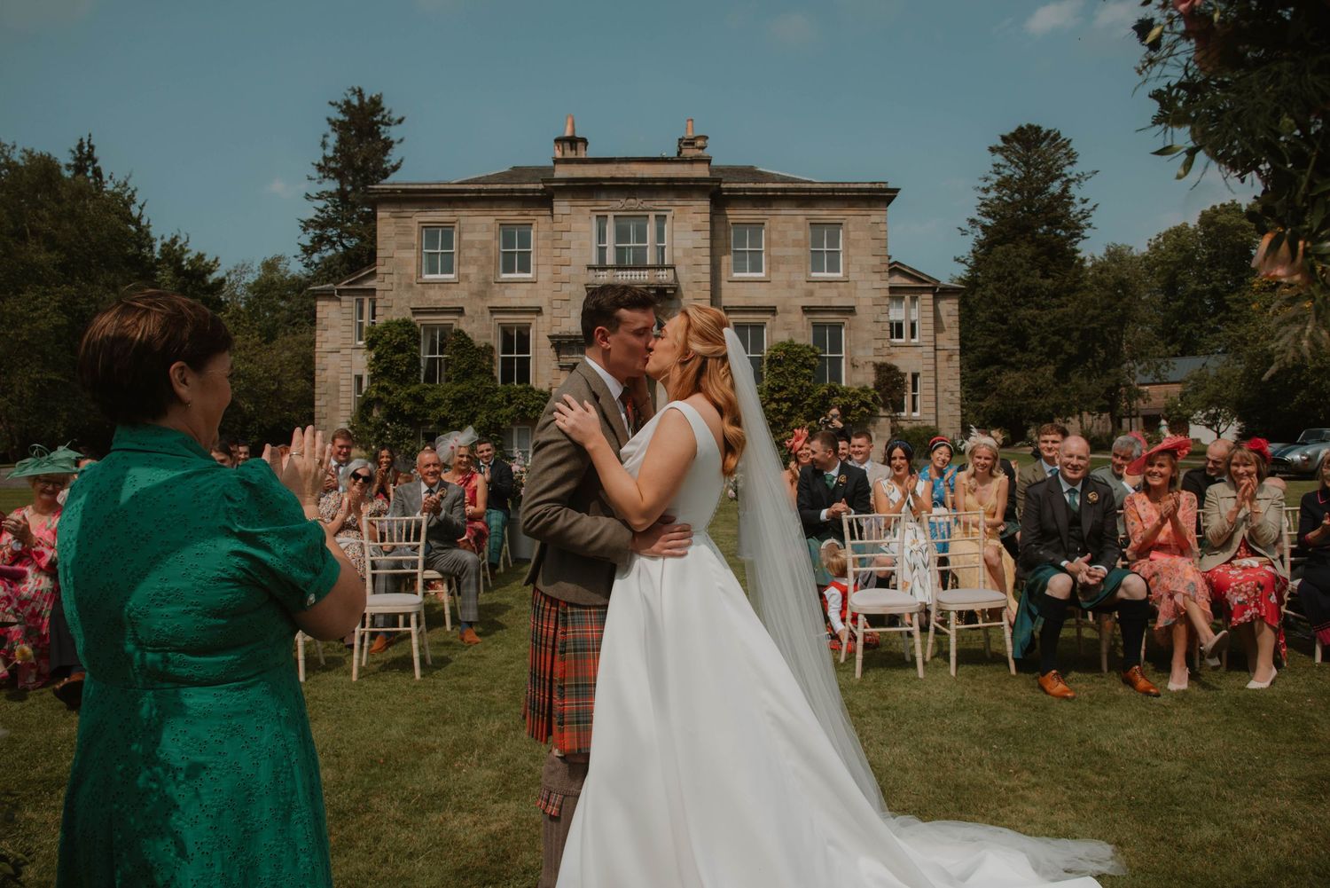 Outdoor garden wedding ceremony setup with chairs and guests on sunny day.