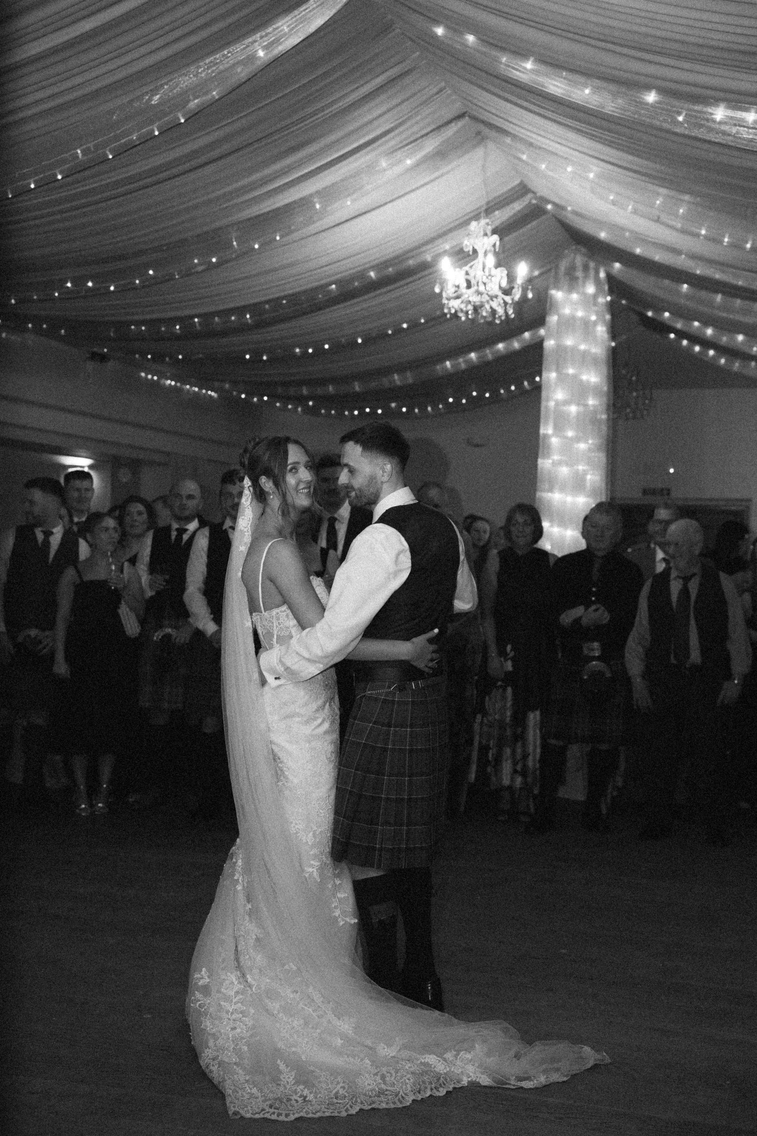 Wedding couple performs romantic dance under elegant draped ceiling with sparkling lights.