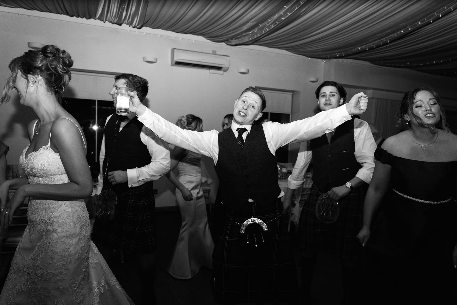 Energetic party scene with people dancing under draped ceiling decorations and string lights.