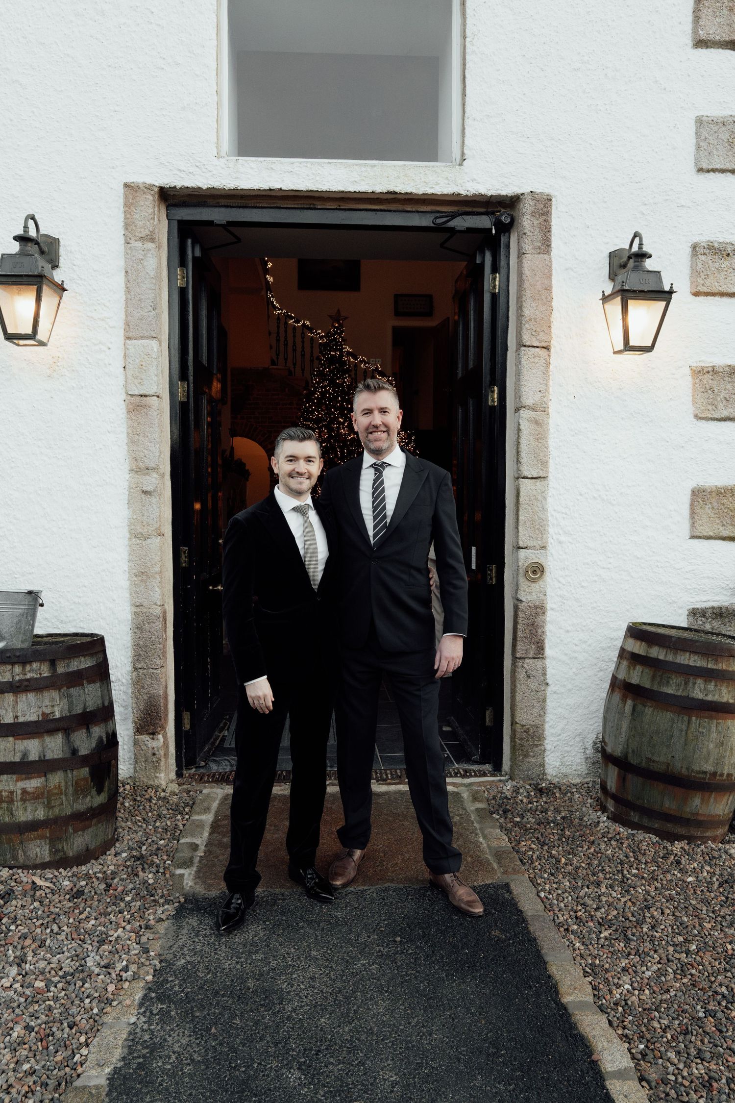 Formal portraits taken outside stone building entrance with wooden barrel decor.
