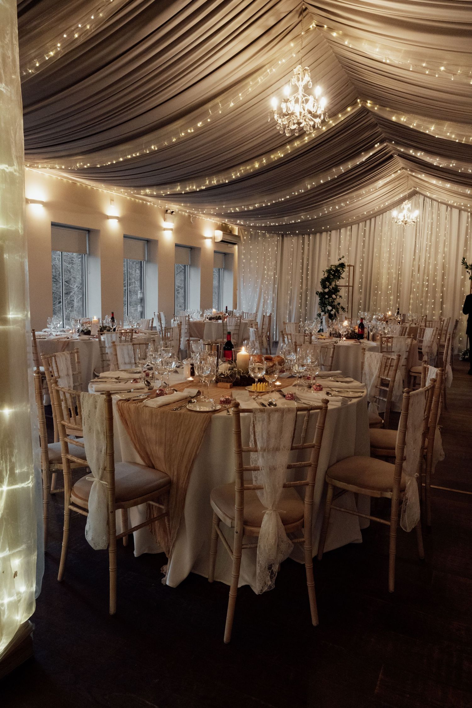 Luxurious wedding reception venue with draped fabric ceiling, chandeliers and round tables.