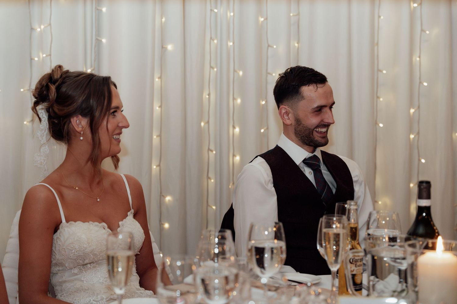 Wedding reception guests seated at tables with wine glasses and string lights creating a warm ambiance.