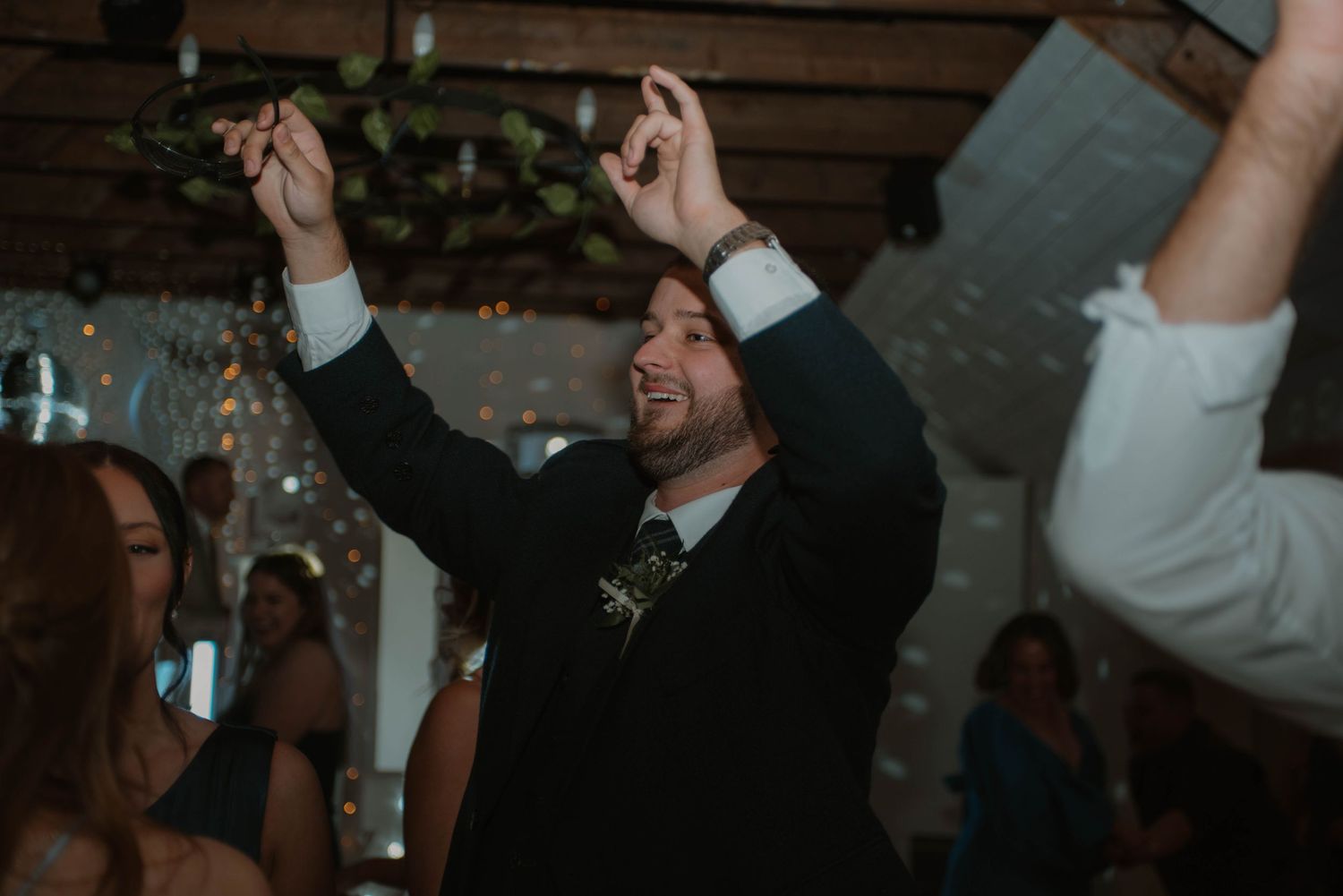Wedding reception party scene with guests celebrating and raising hands on dance floor.