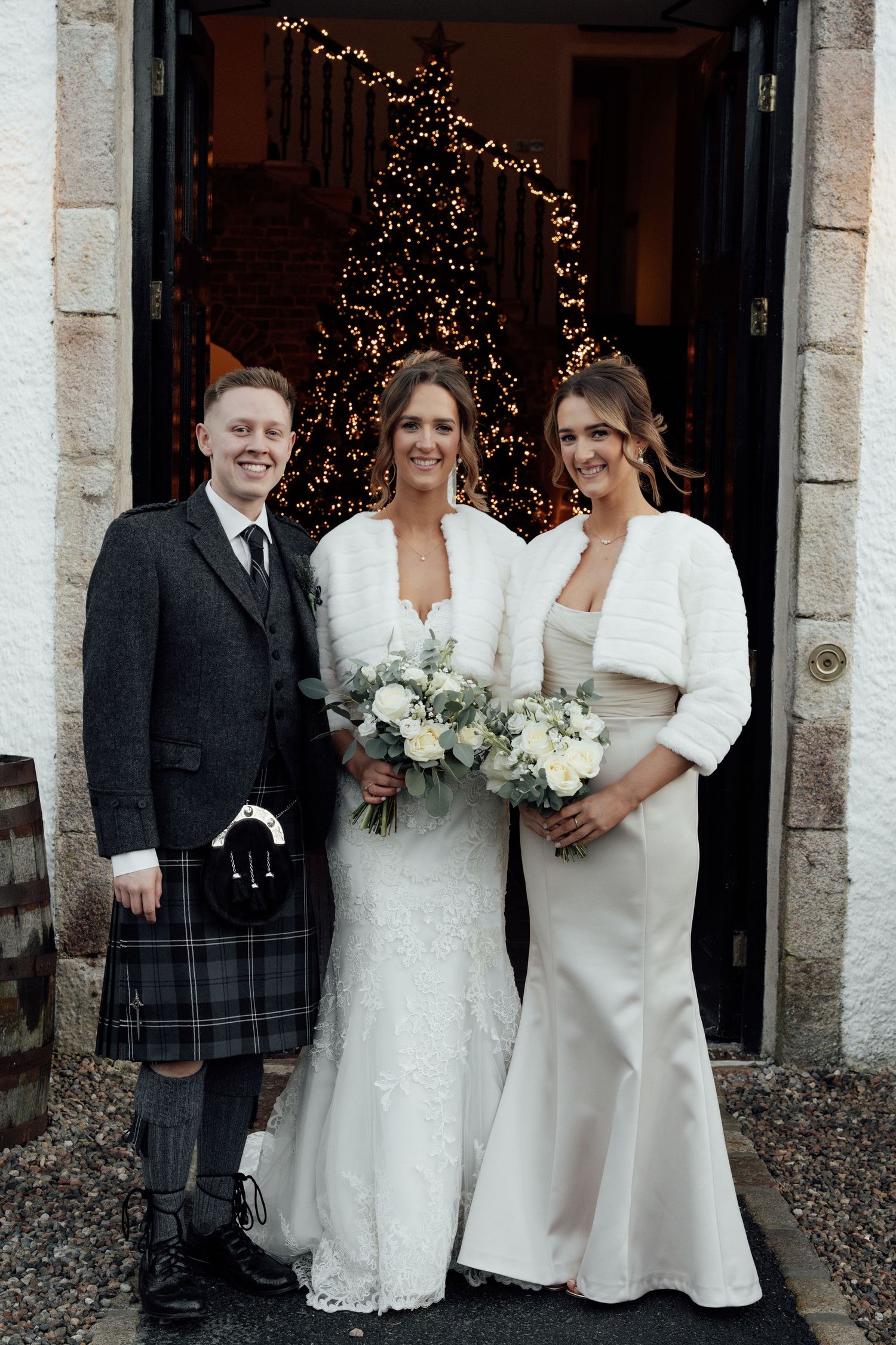 Wedding celebration group with traditional Scottish kilt and formal attire outside decorated venue entrance.
