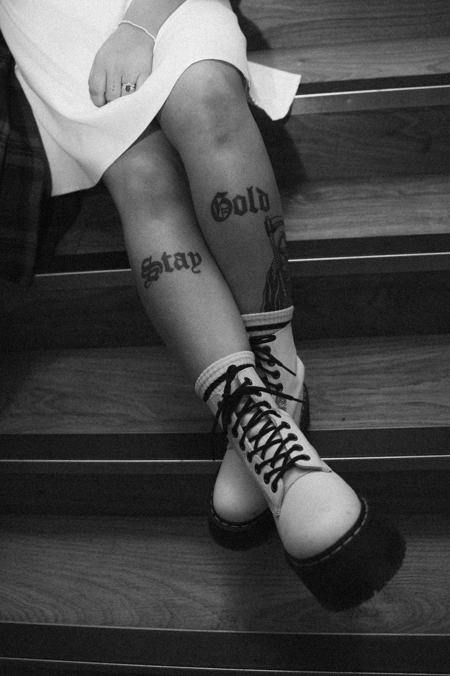 Close-up of bride's legs showing Stay Gold tattoos wearing white Dr. Martens boots on stairs.