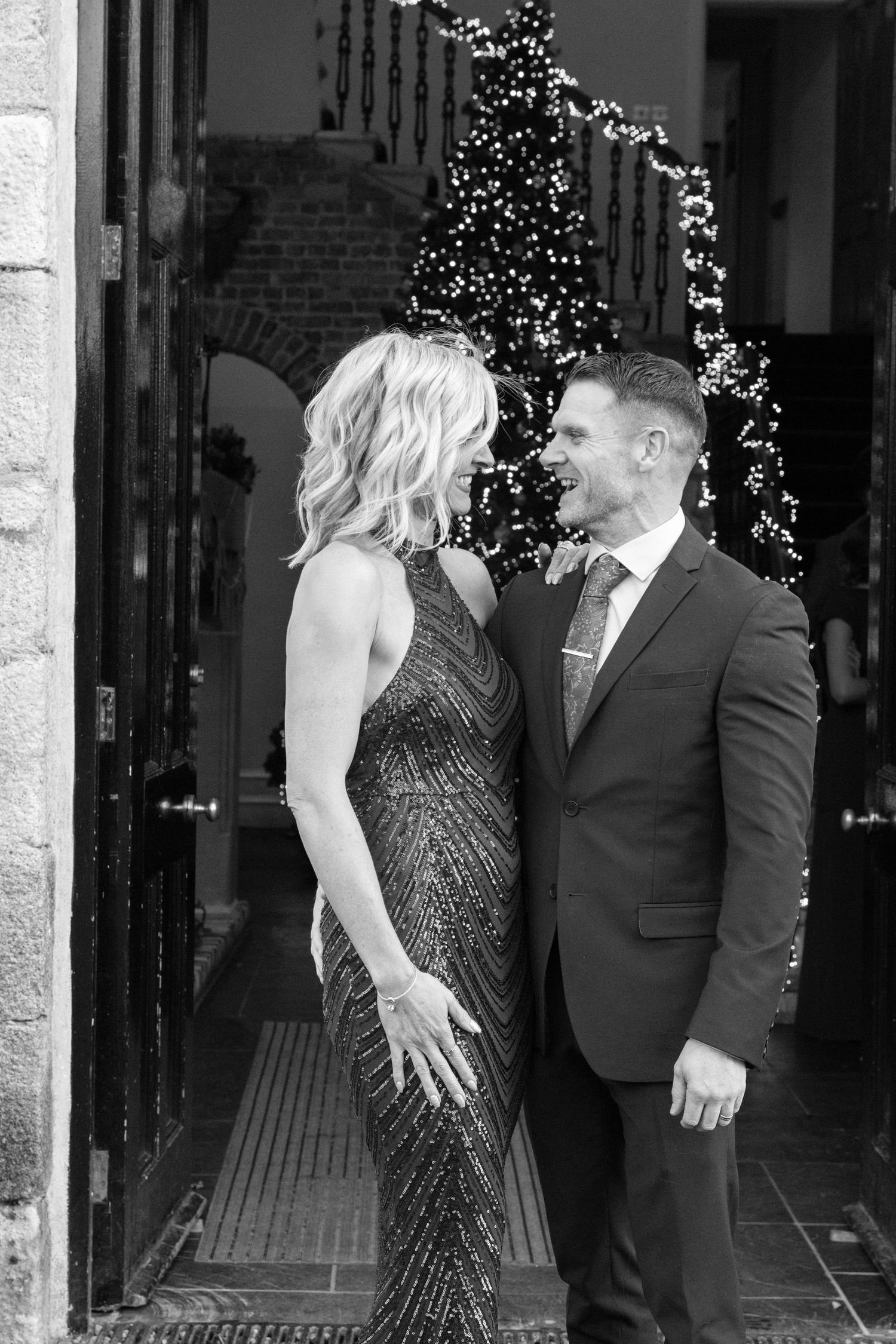 A couple shares an intimate moment in front of a venue entrance with twinkling lights.