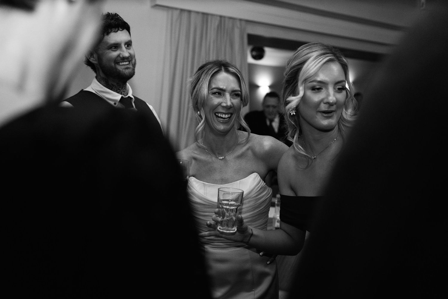 Black and white photo capturing candid moments of laughter at a wedding reception.