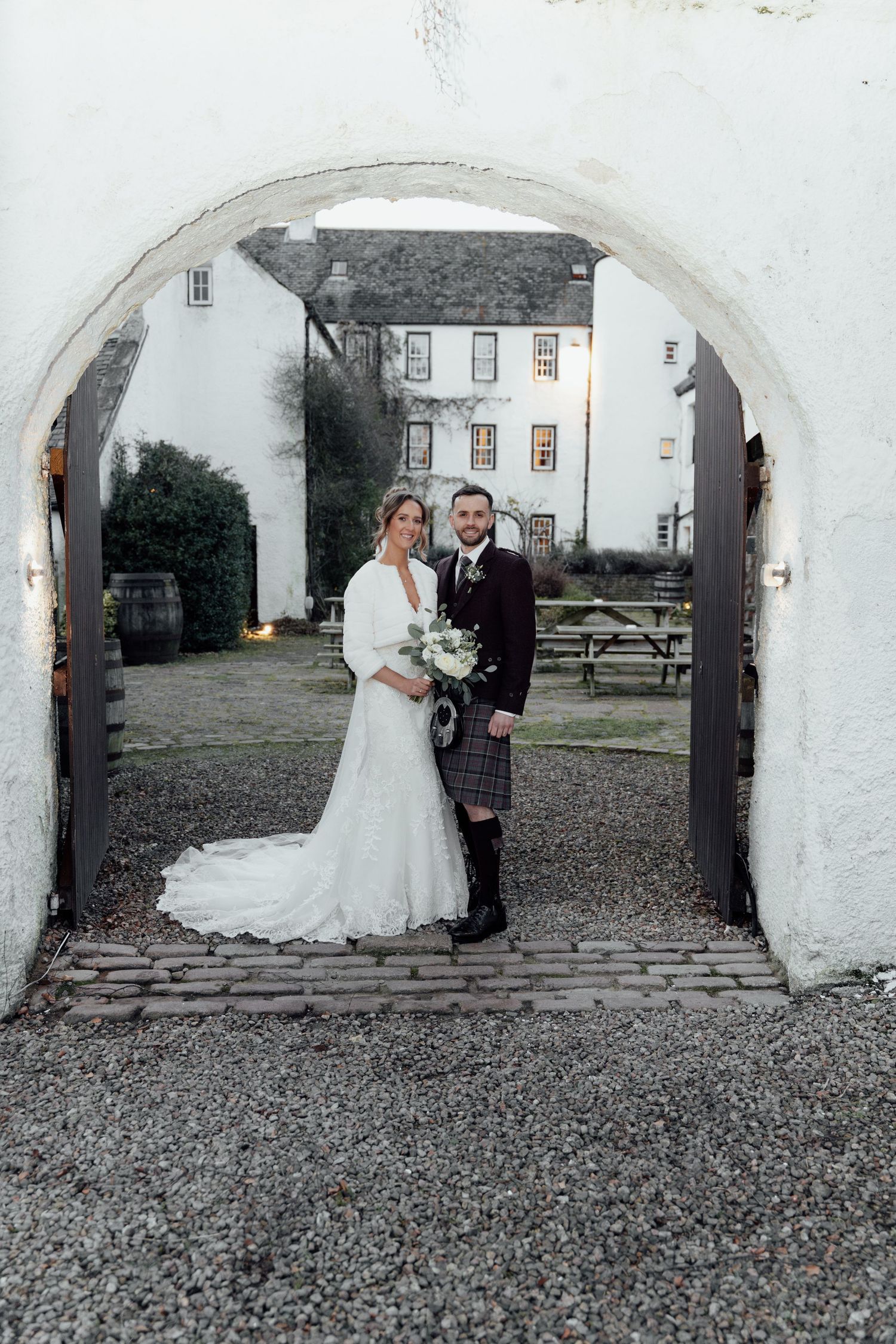 Traditional Scottish wedding portrait under white stone archway.