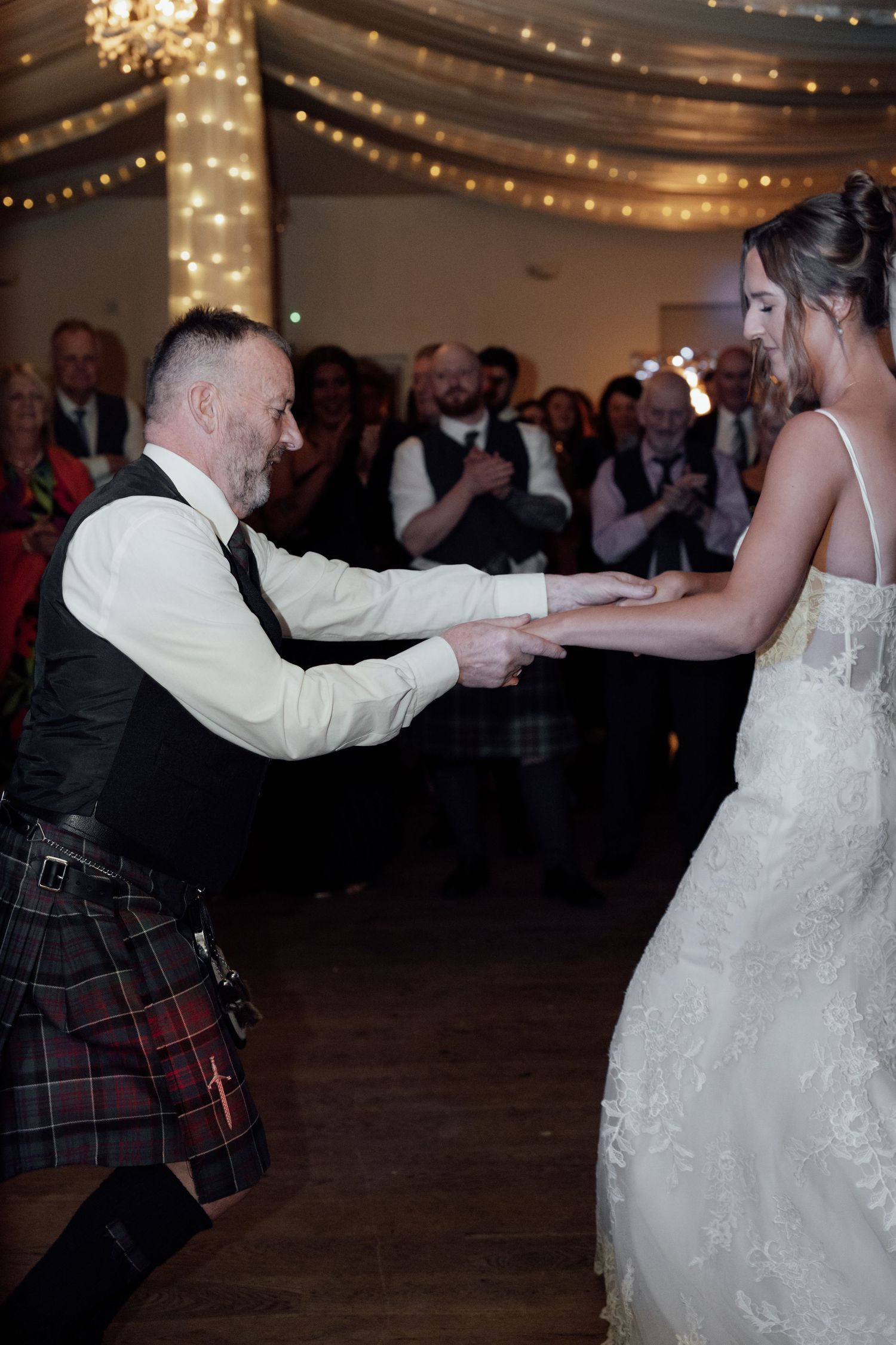 Newlyweds dance together in a reception hall with Scottish kilts and white wedding dress.