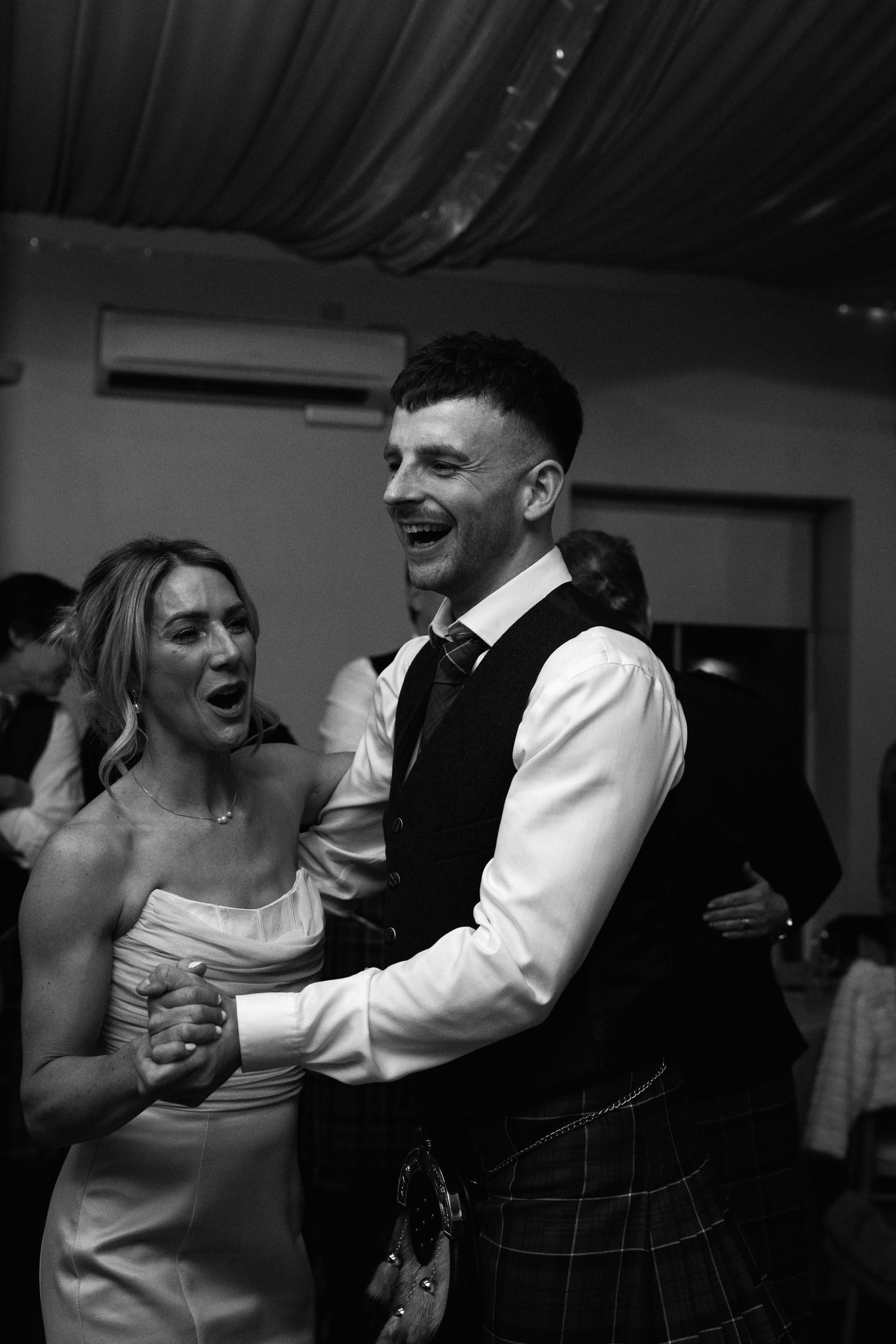 A couple shares a joyful dance moment at a wedding reception under dim lighting.