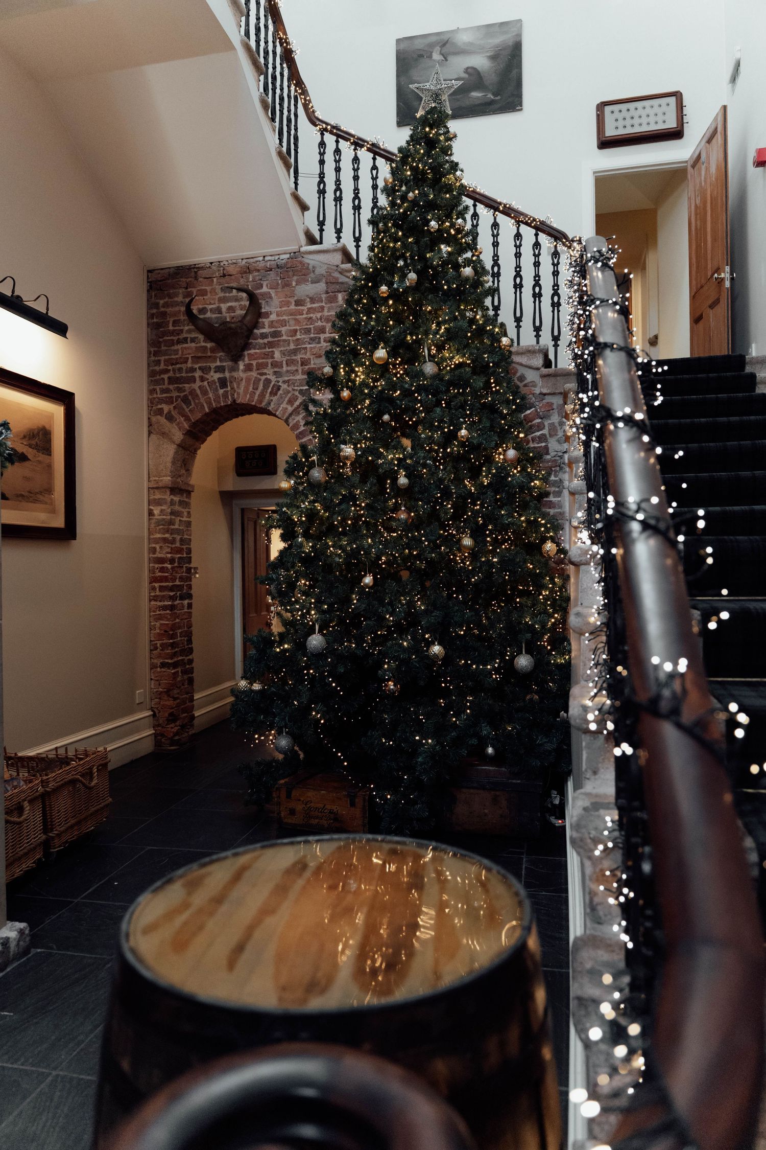 Christmas tree and fairy lights decorate elegant indoor staircase with brick archway.