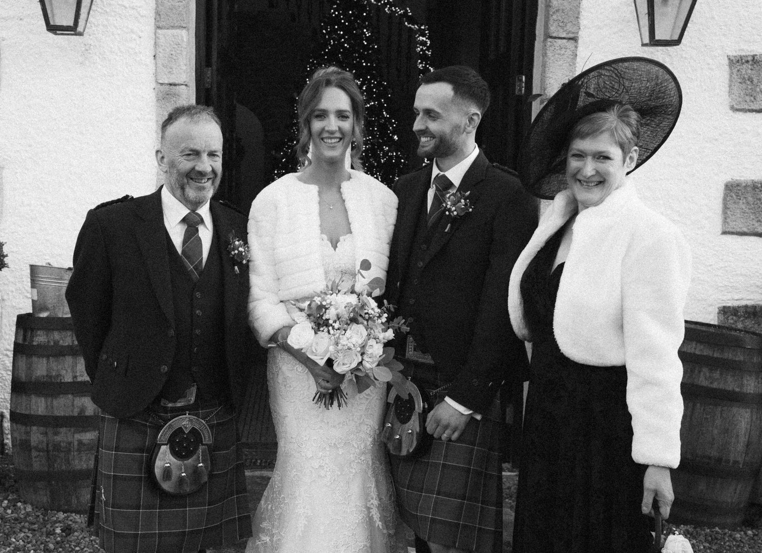 Wedding group gathered by doorway with kilts and white dress in monochrome style.