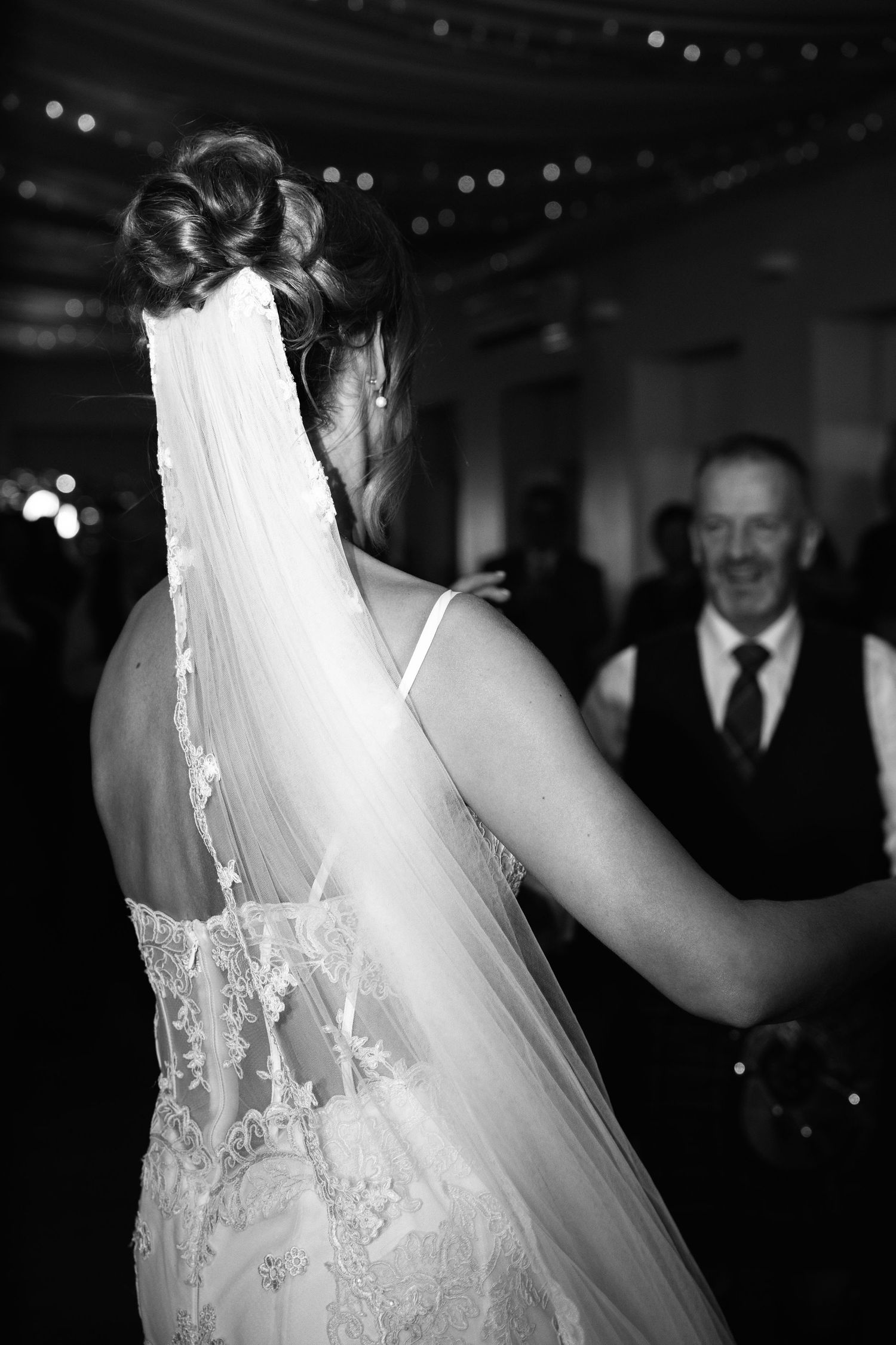 Detailed lace back of a wedding dress with flowing veil captured during a reception dance.