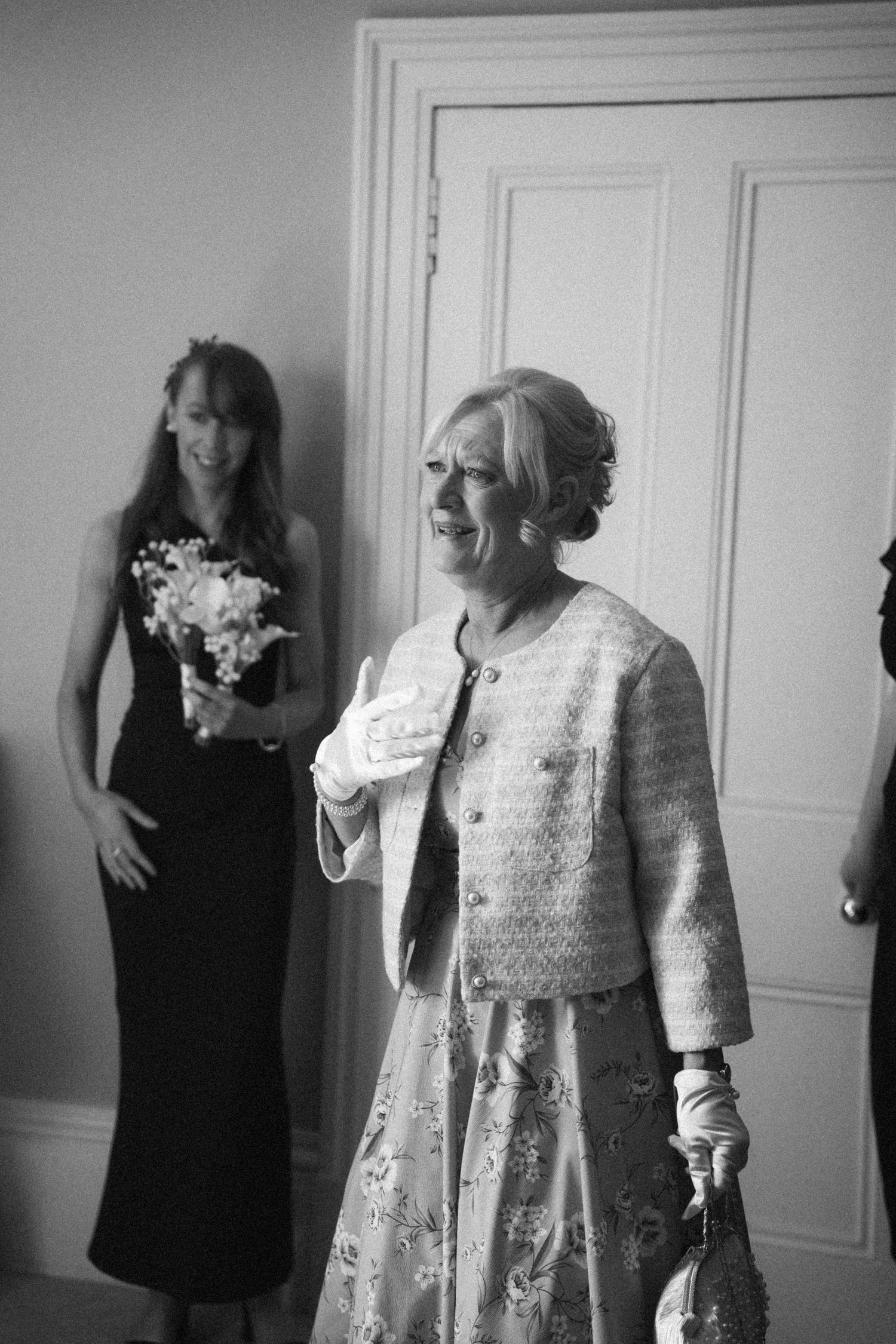 Elegant older woman in embroidered suit emotional at wedding ceremony in black and white photo.