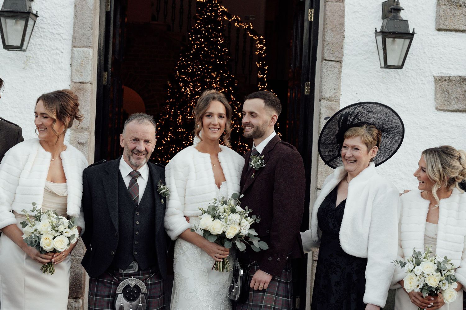 Wedding party members sharing candid moments outside stone building with traditional lanterns.