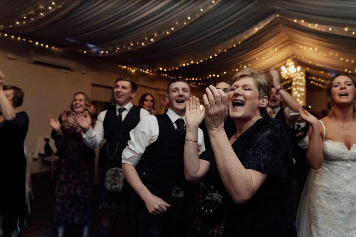 Wedding guests dancing and celebrating with joy under elegant draped ceiling.