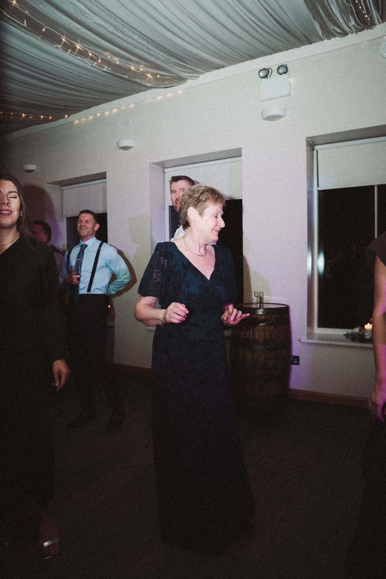 Dark reception venue with guests dancing under fabric-draped ceiling and string lights.