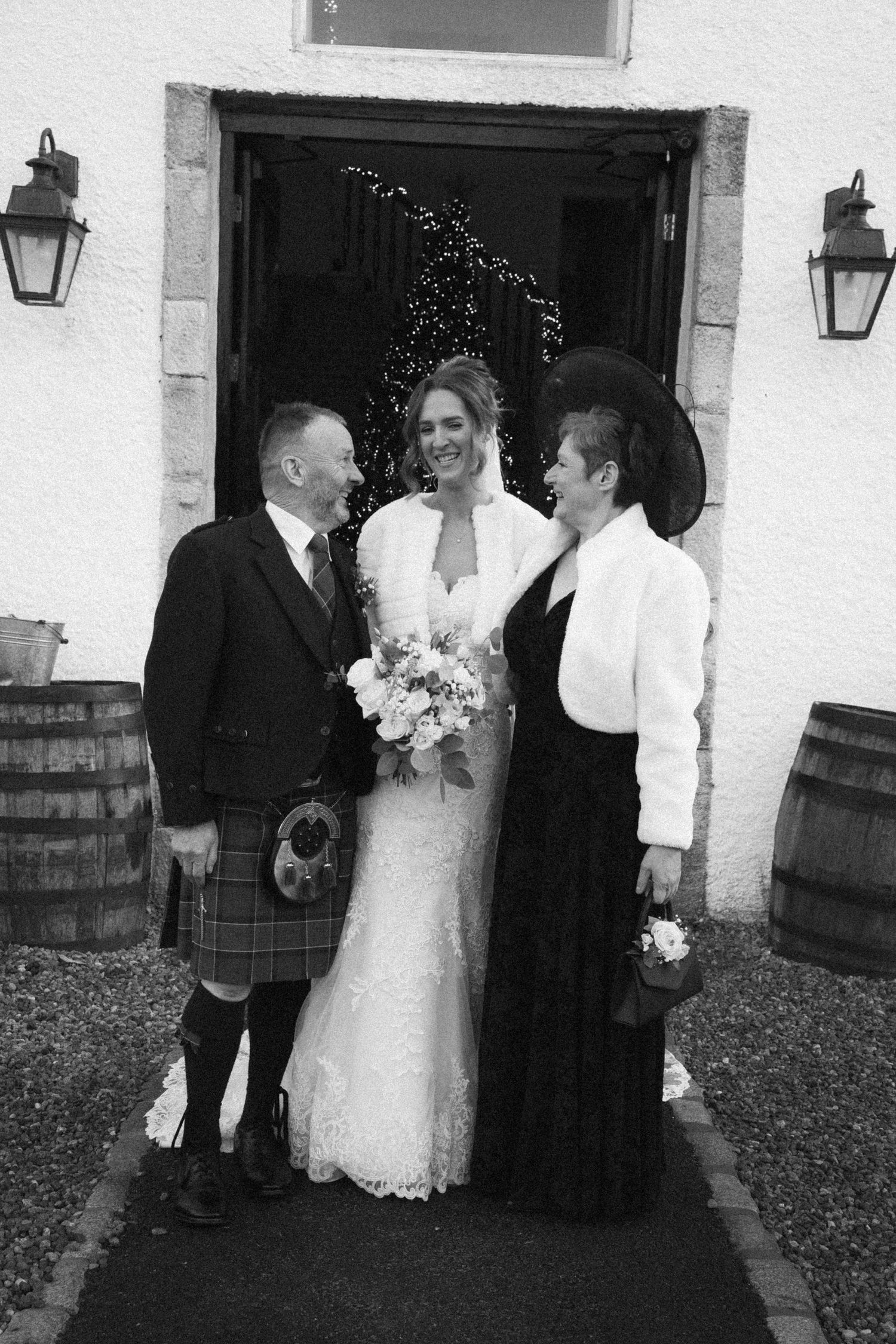 Black and white wedding photo of group gathered by doorway with traditional Scottish attire.