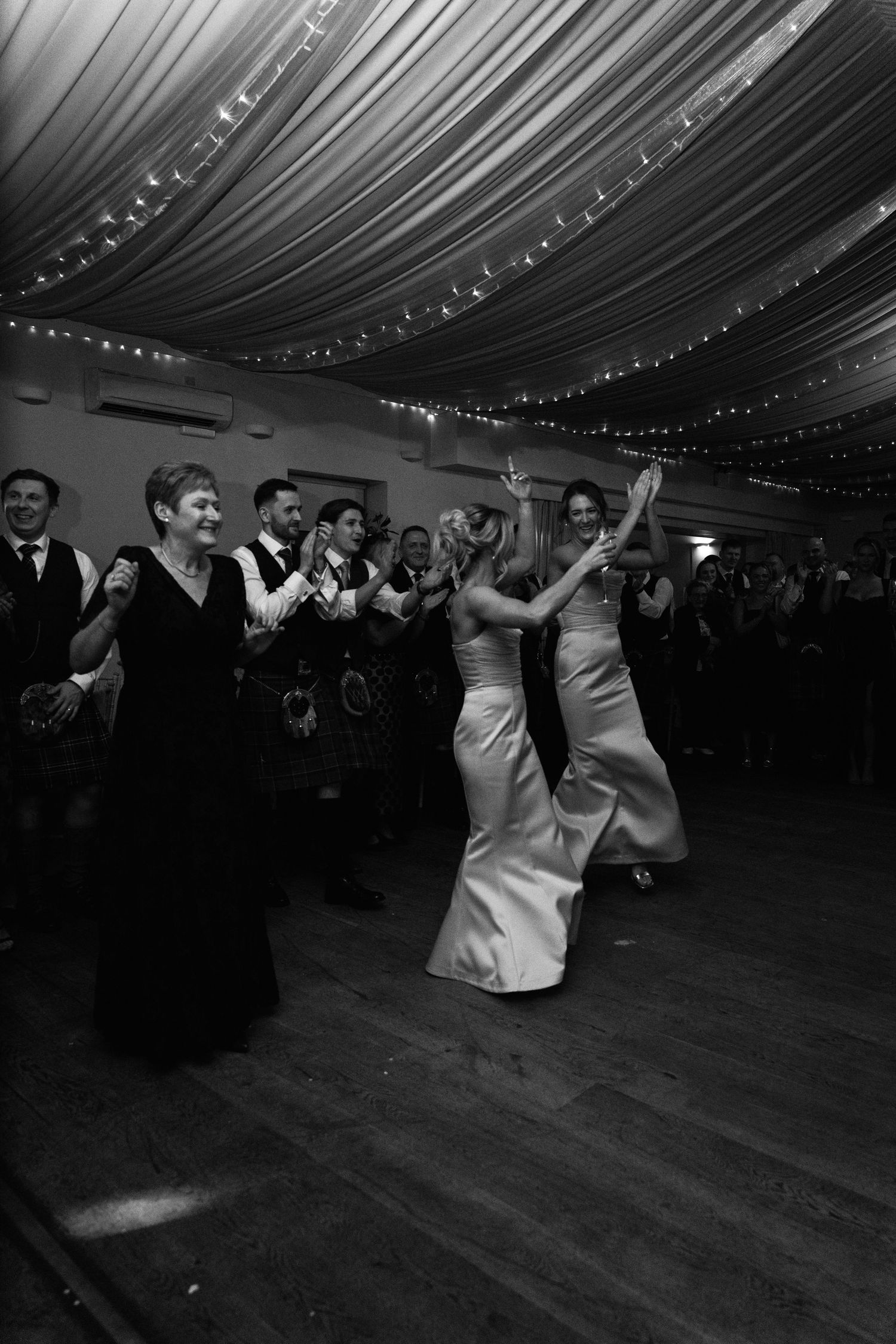 Wedding celebration features dancing couples under elegant draped ceiling with twinkle lights.