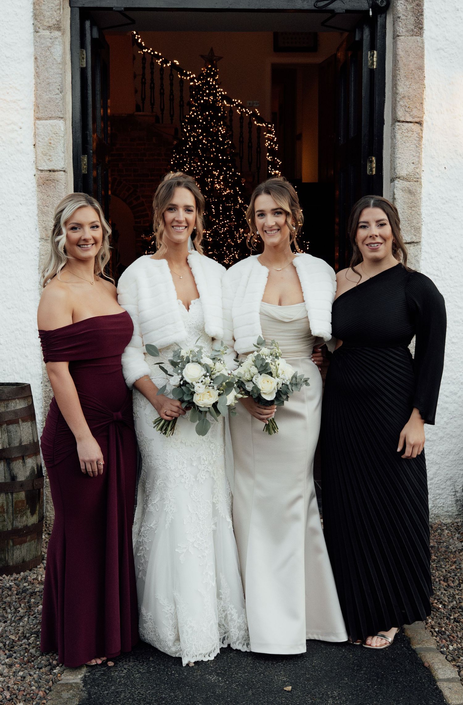Bridesmaids in burgundy and black dresses pose with brides holding white bouquets.
