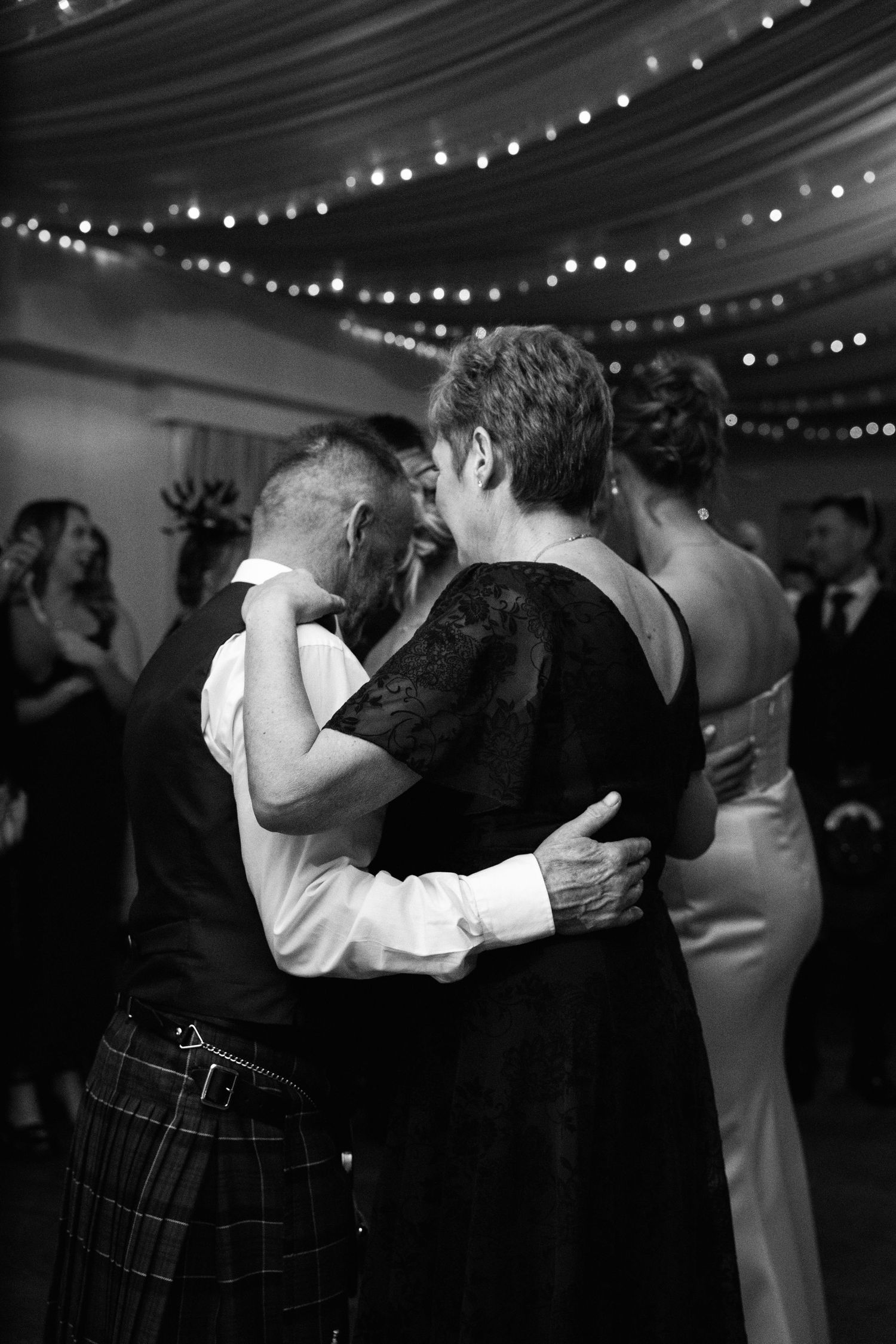 Intimate dance moment captured in black and white under string lights at wedding reception.