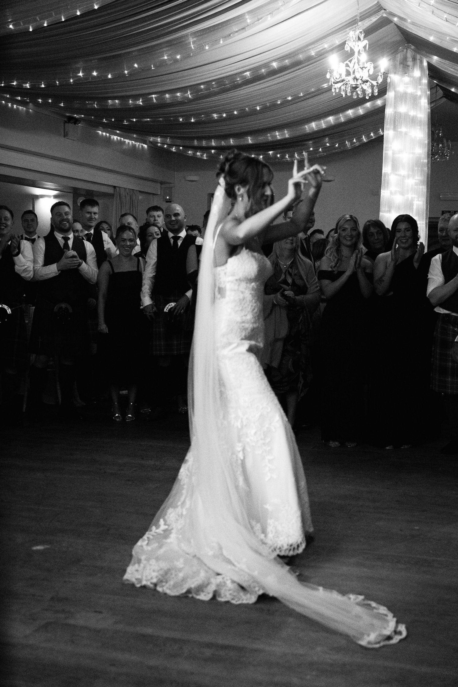 A couple performs their first dance at a wedding reception under draped fabric ceiling and string lights.