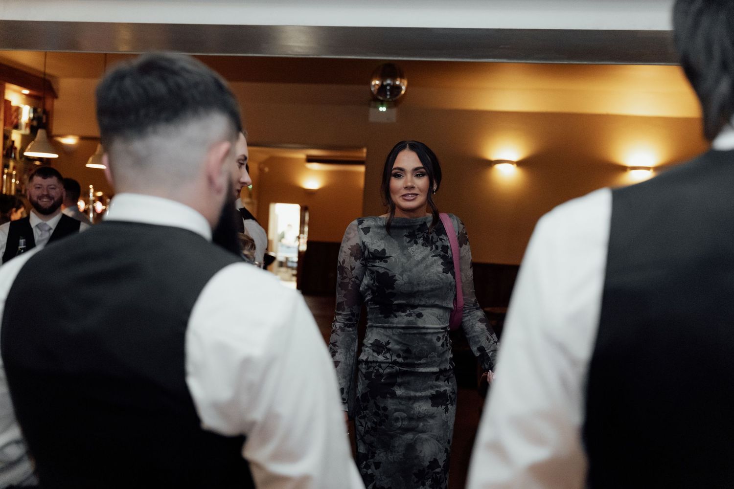 Wedding guests mingle and socialize in formal attire at an indoor venue.