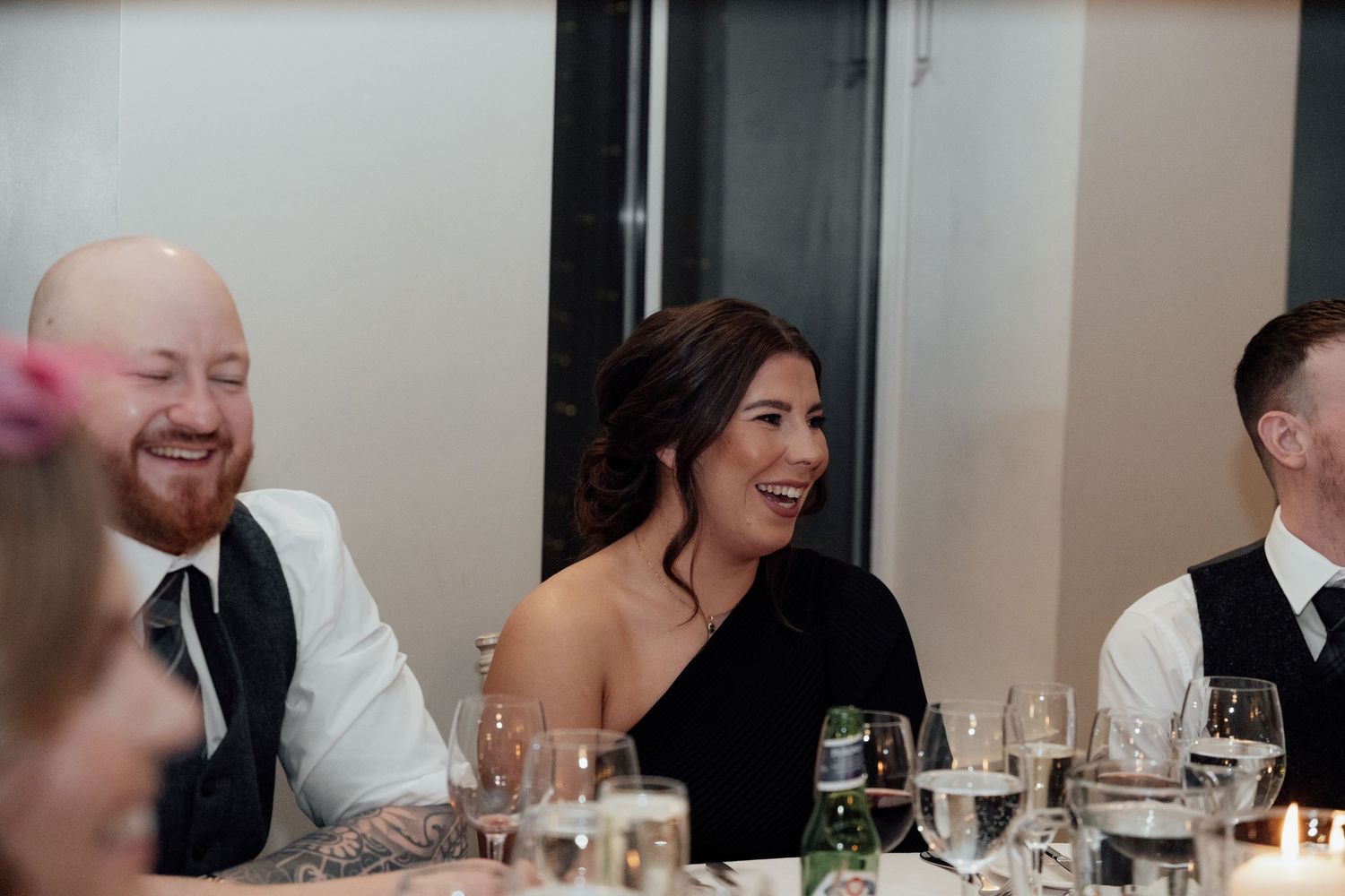 Wedding reception guests enjoying dinner and conversation under soft lighting.
