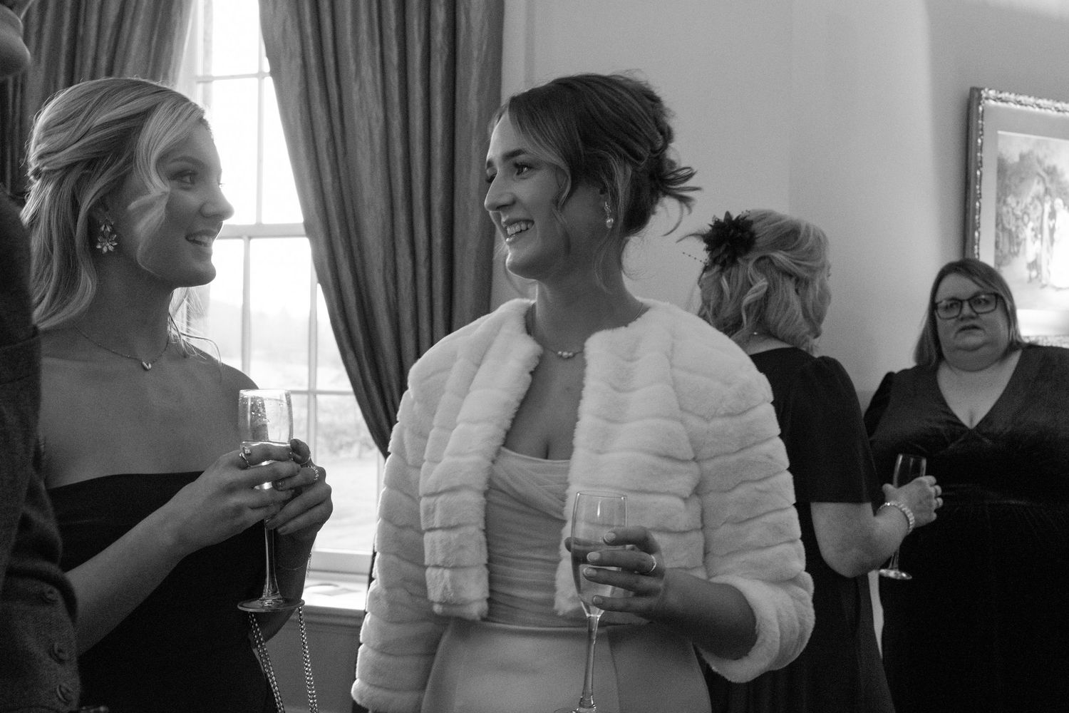 Black and white photograph of guests enjoying drinks at an indoor event.