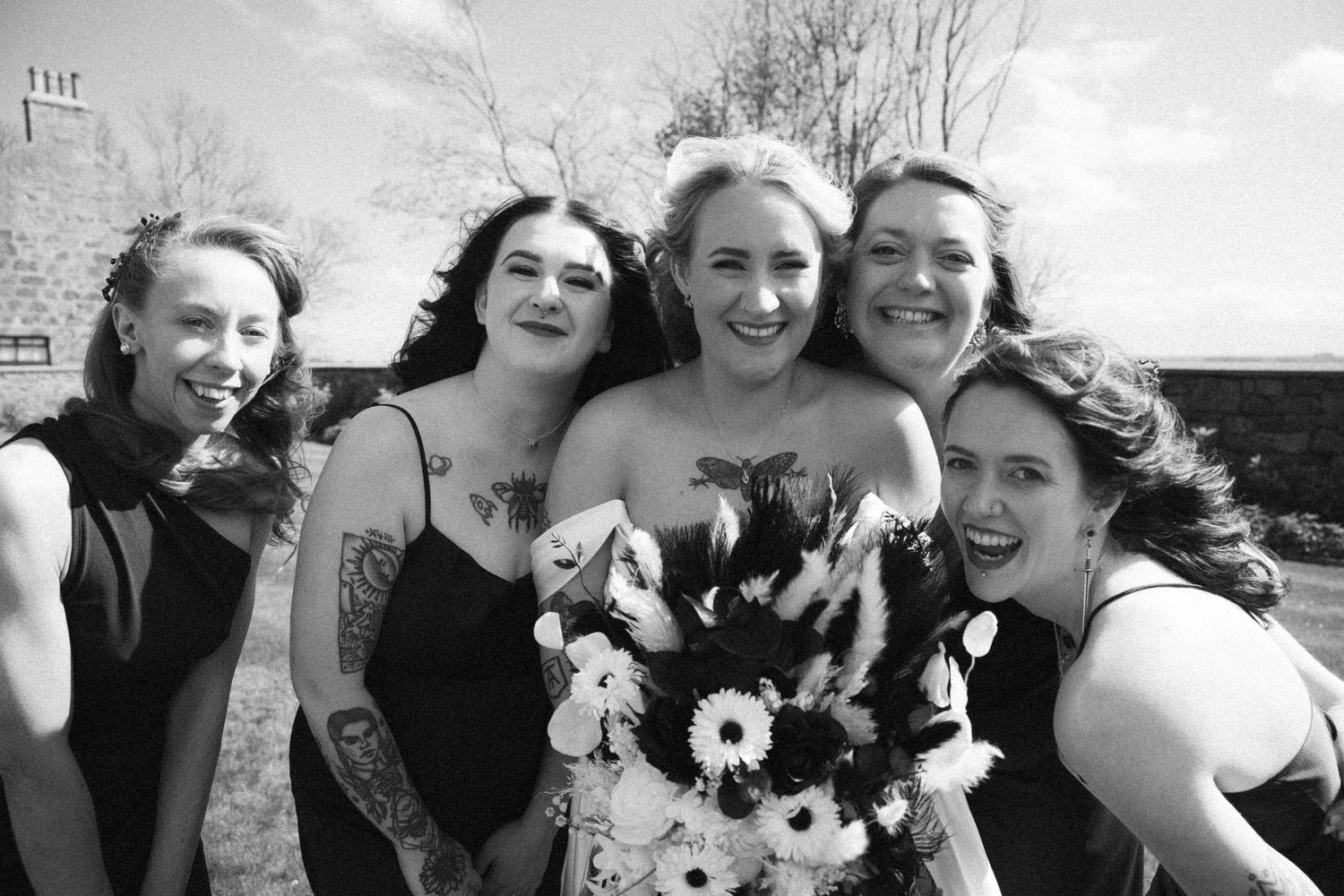 Bride and four bridesmaids laughing together in black and white outdoor wedding photo.