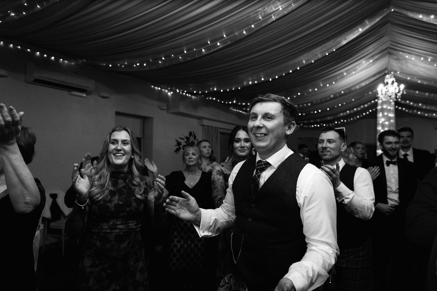 Guests celebrating at wedding reception under draped fabric ceiling with twinkle lights.