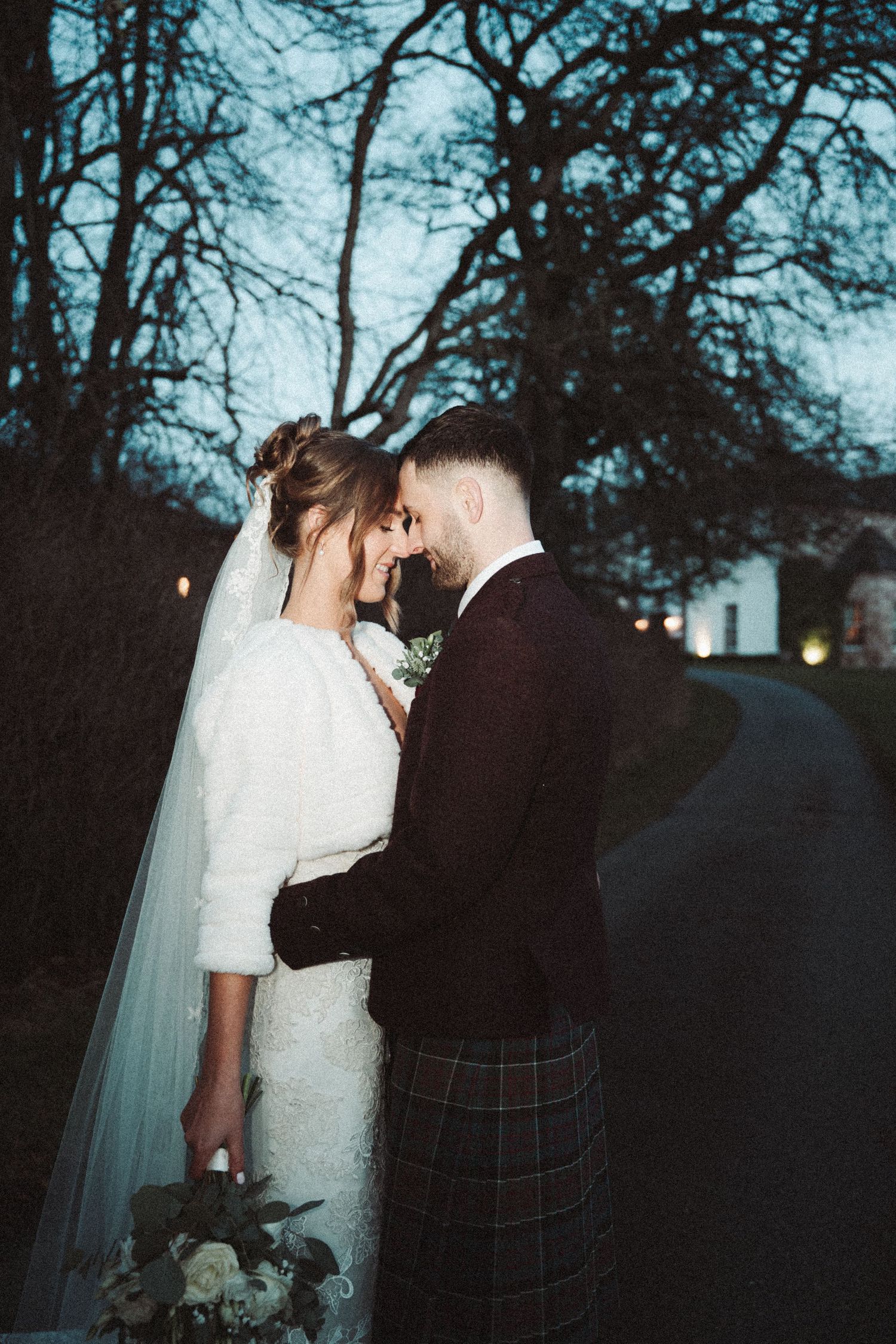 Wedding couple shares intimate moments in a garden setting with the bride in white and groom in traditional kilt.