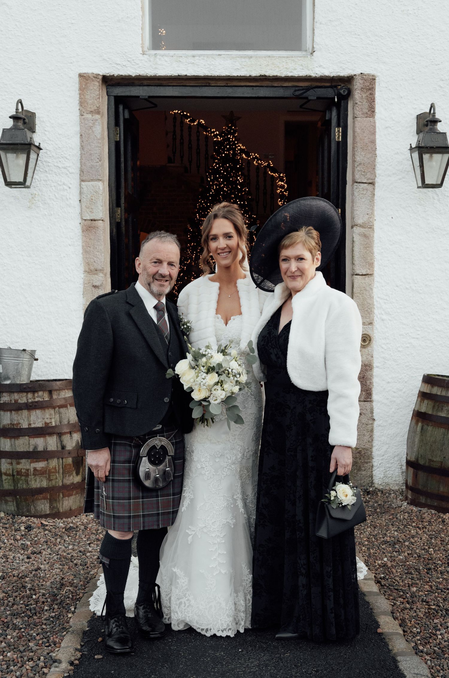 Formal wedding group photo with Scottish kilts and white bridal gown by building entrance.