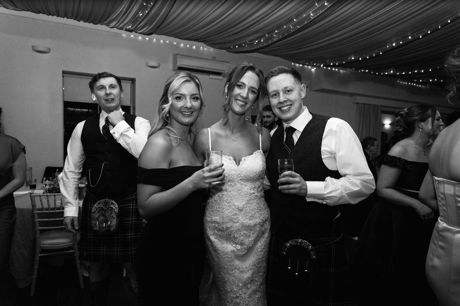 Wedding party dancing and celebrating in formal attire under draped ceiling decorations.