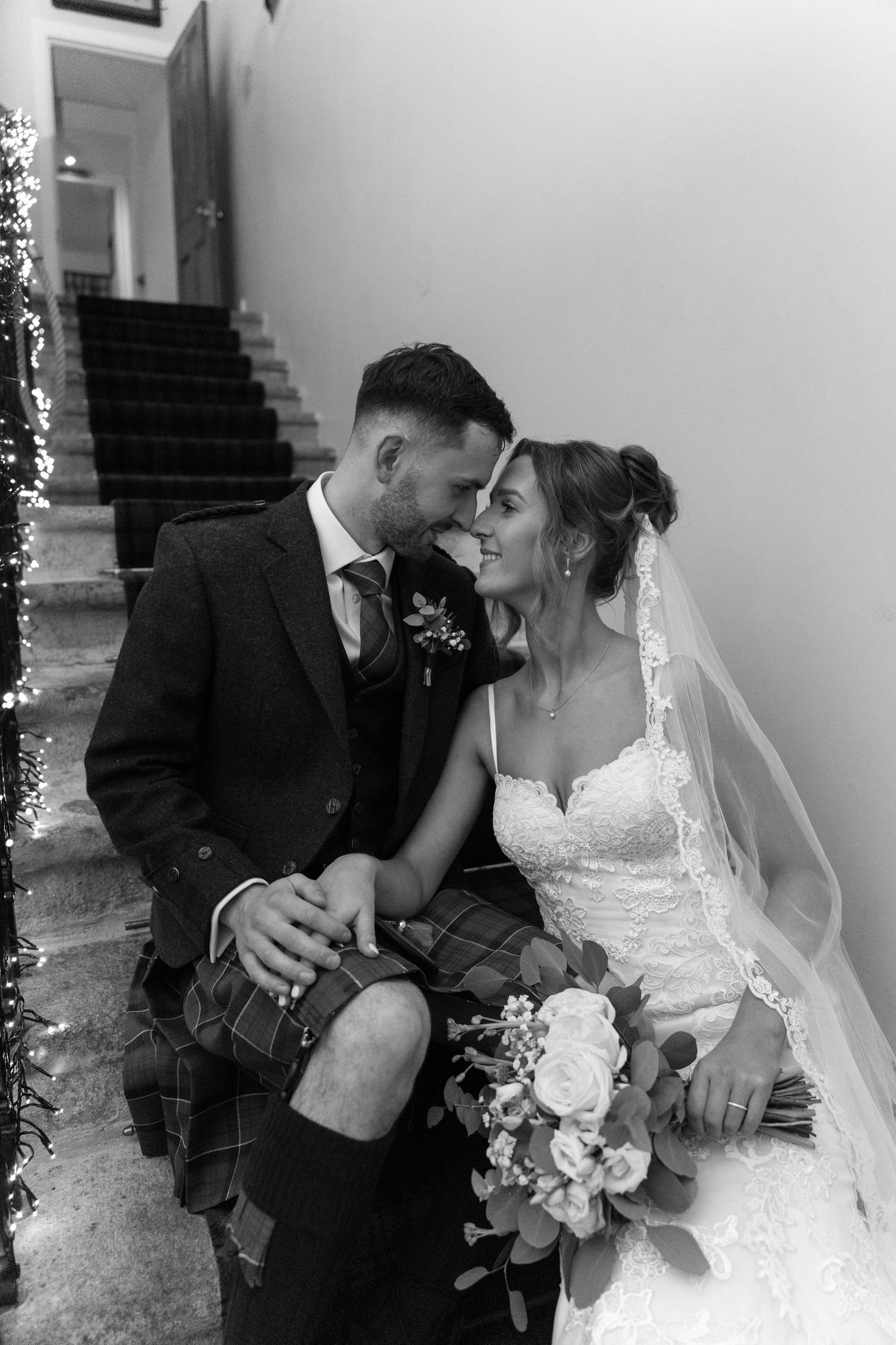 Black and white romantic moment captured on stairs with bride holding white floral bouquet.