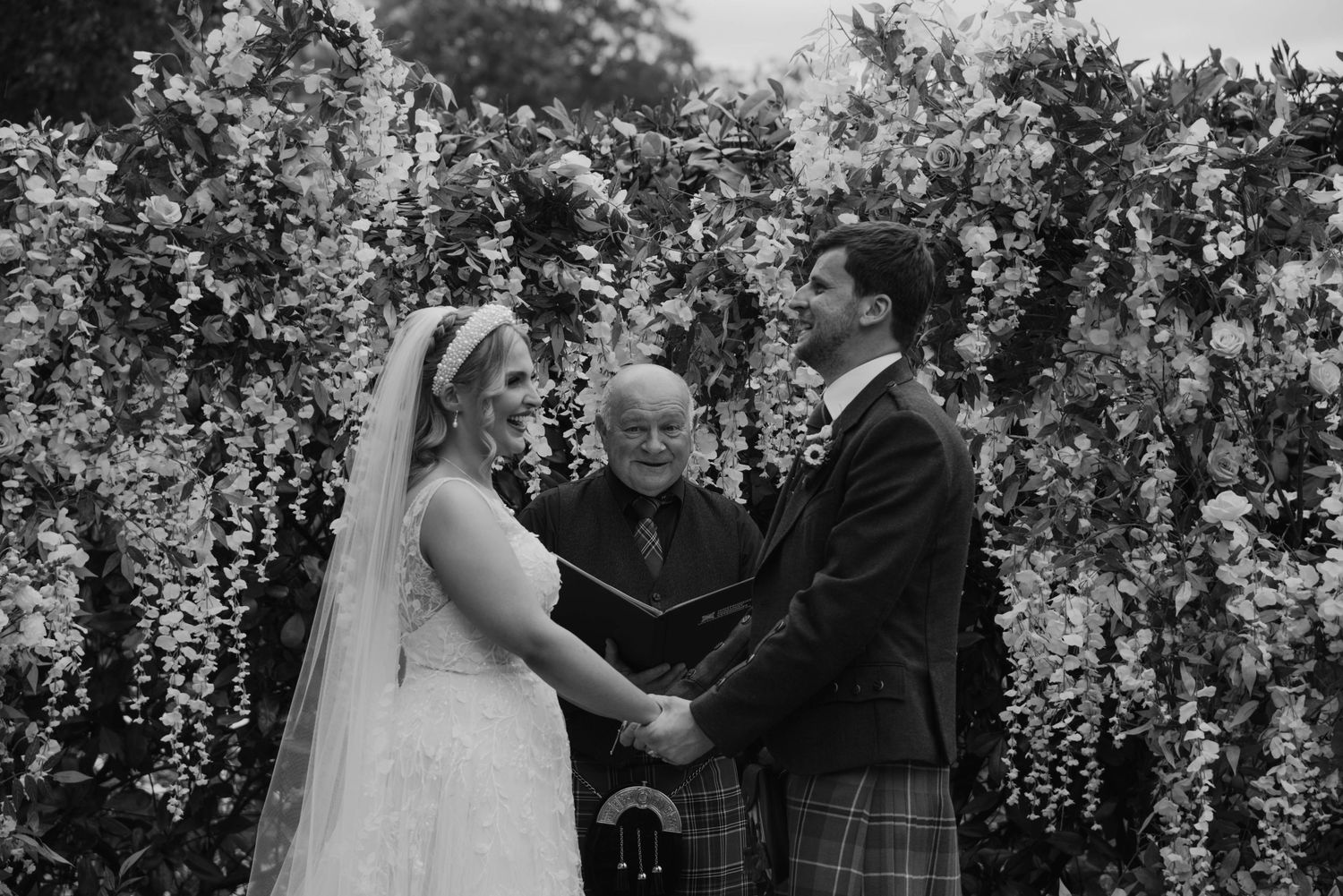Outdoor wedding ceremony with floral arch and natural garden setting.