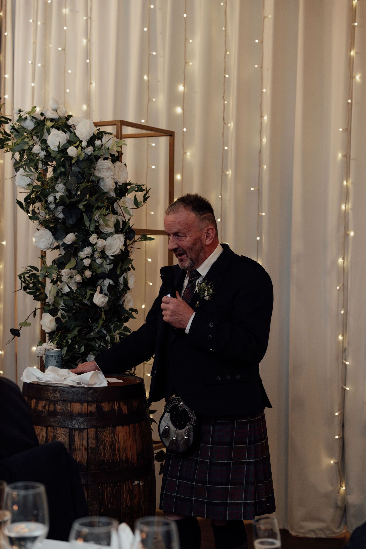 A wedding reception venue decorated with fairy lights and white floral arrangements on wine barrels.