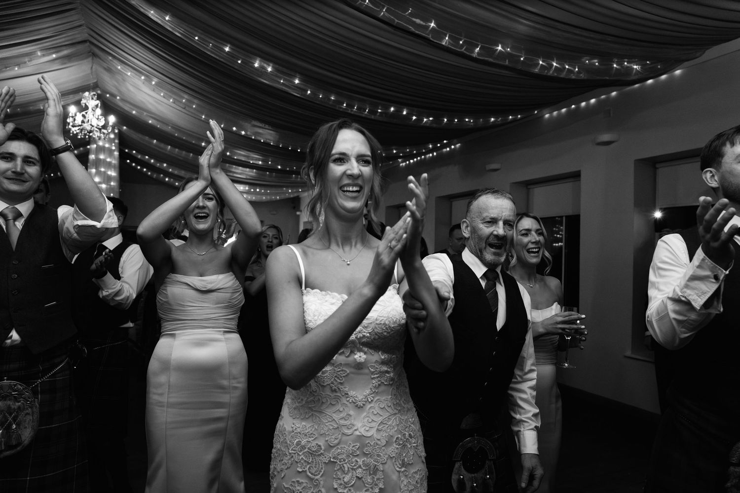 Guests celebrating on dance floor beneath elegant black ceiling drapes and fairy lights.