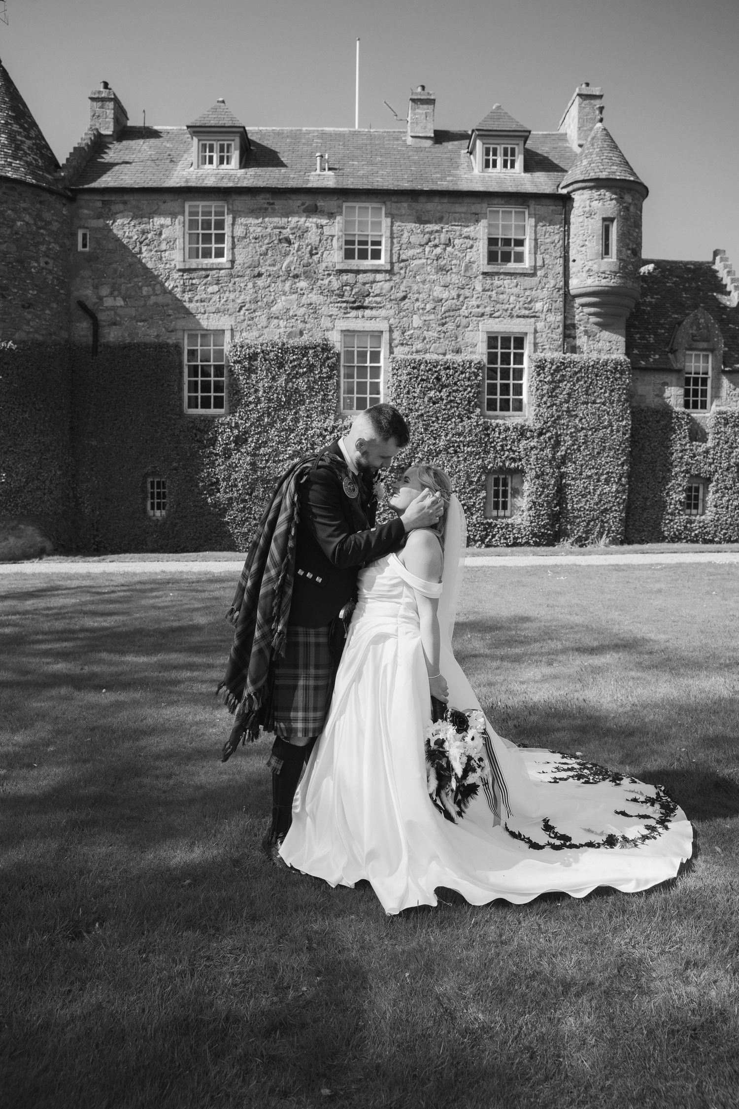 Bride and groom sharing a romantic kiss outside an ivy-covered Scottish castle on their wedding day.
