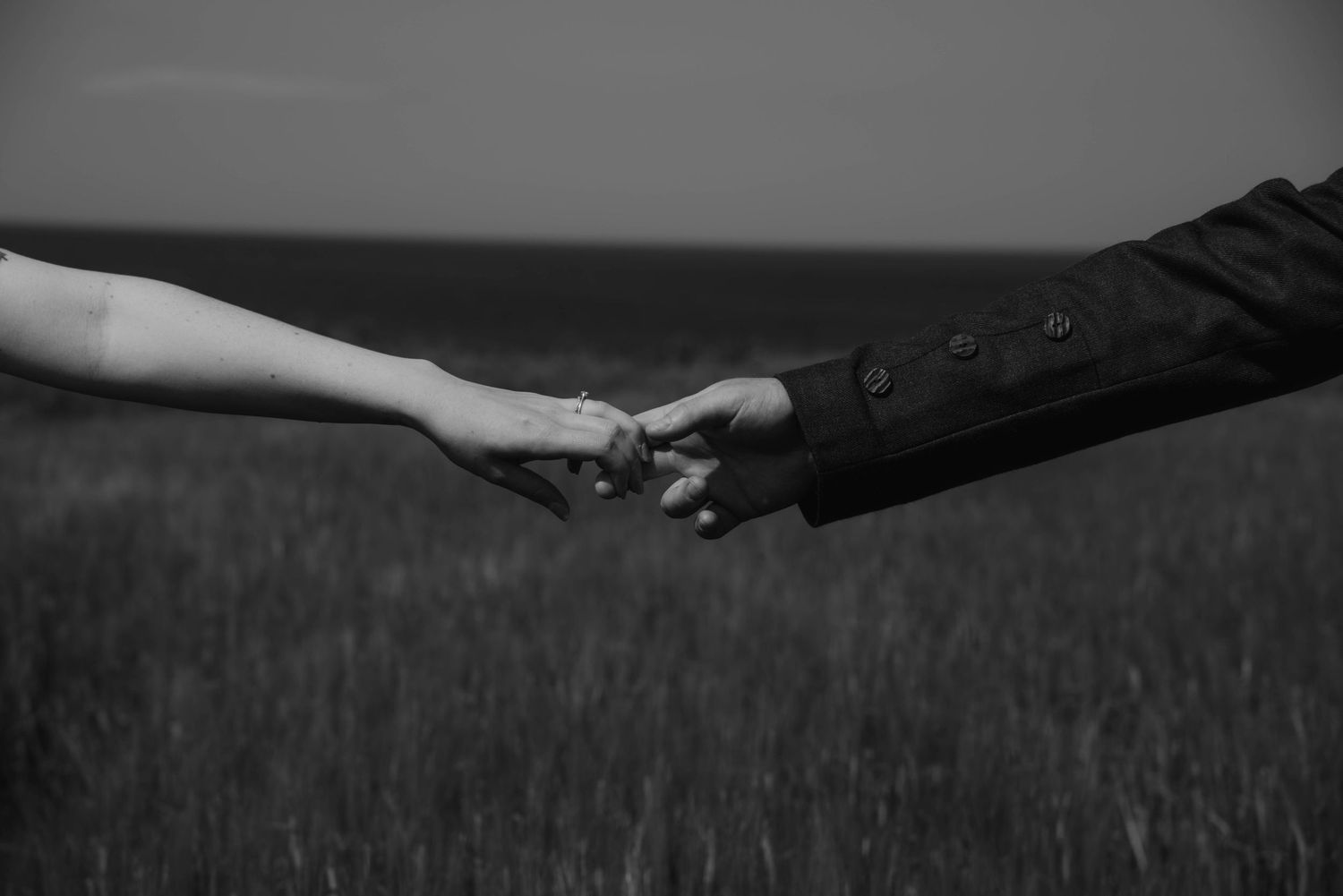 Artistic black and white photo of hands reaching across empty field.