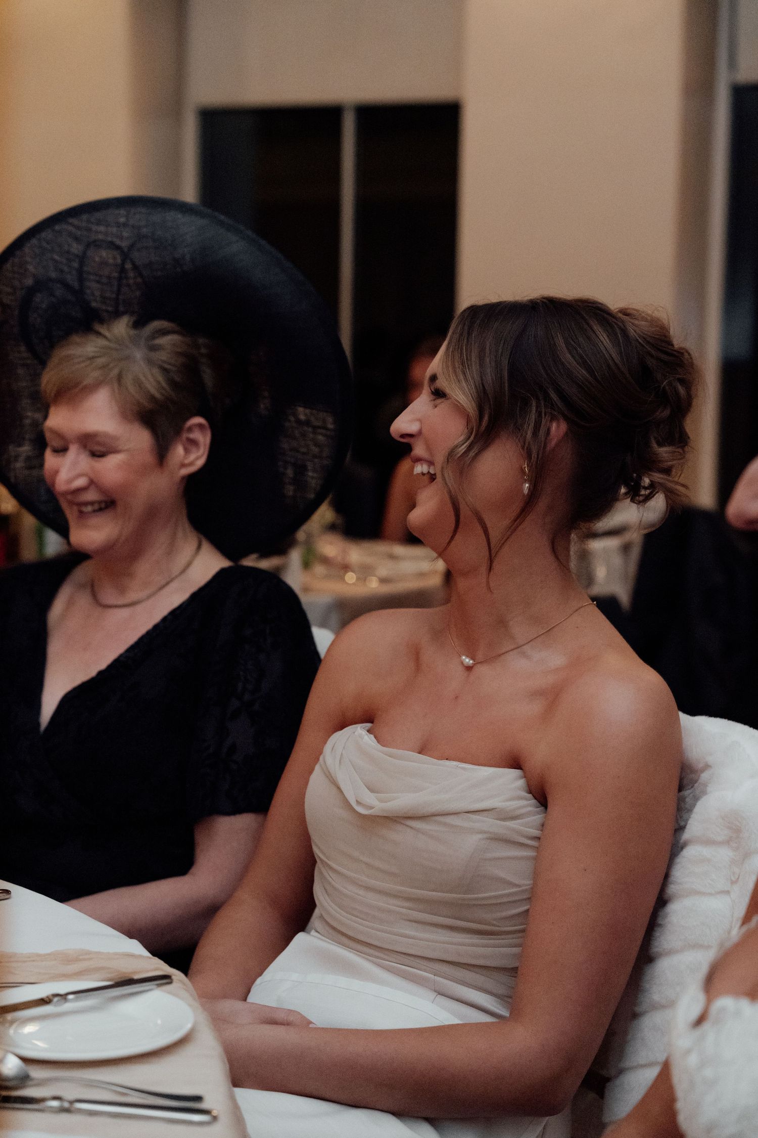 Wedding guests sharing laughter during reception dinner under warm lighting.