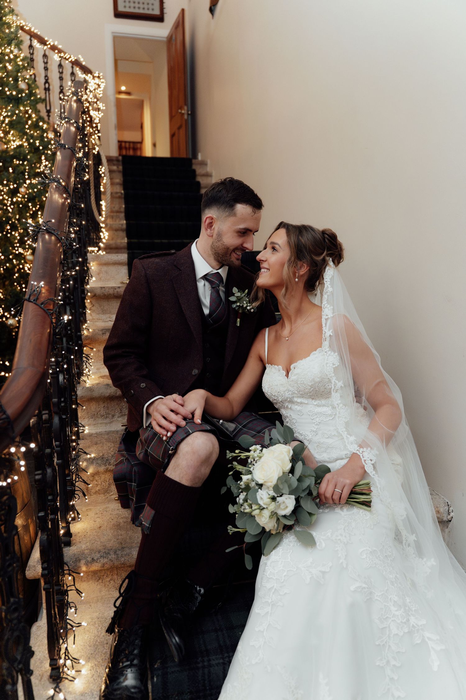 Intimate wedding portrait on staircase with Christmas tree lights creating romantic ambiance.