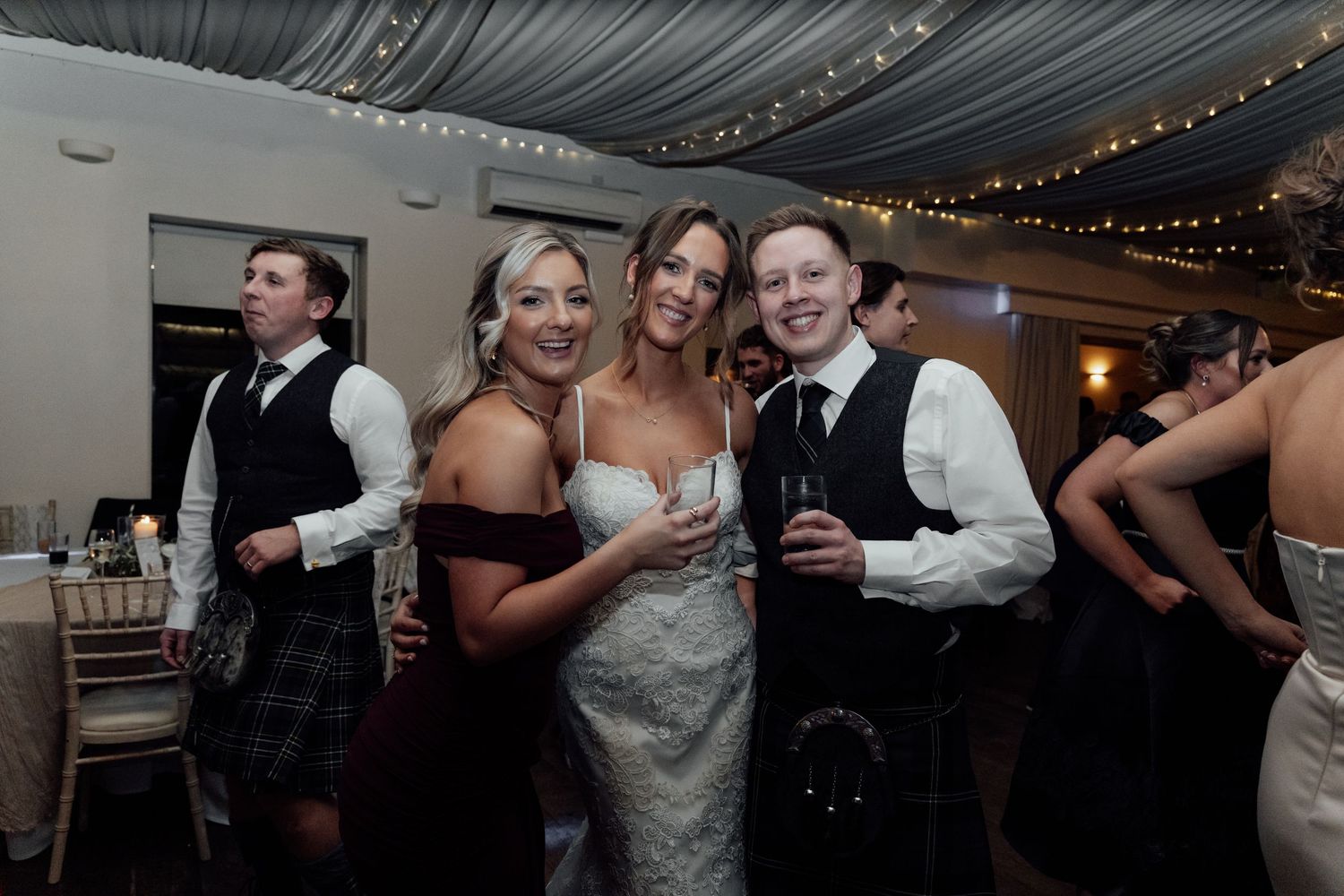 Wedding guests dancing and celebrating under elegant fabric ceiling with string lights.
