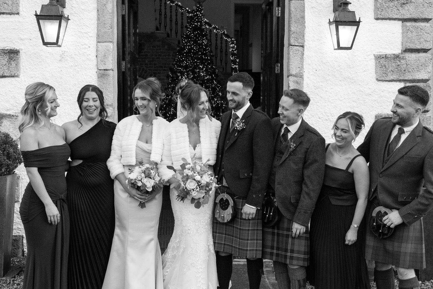 Black and white photo of wedding party members lined up against white building exterior.