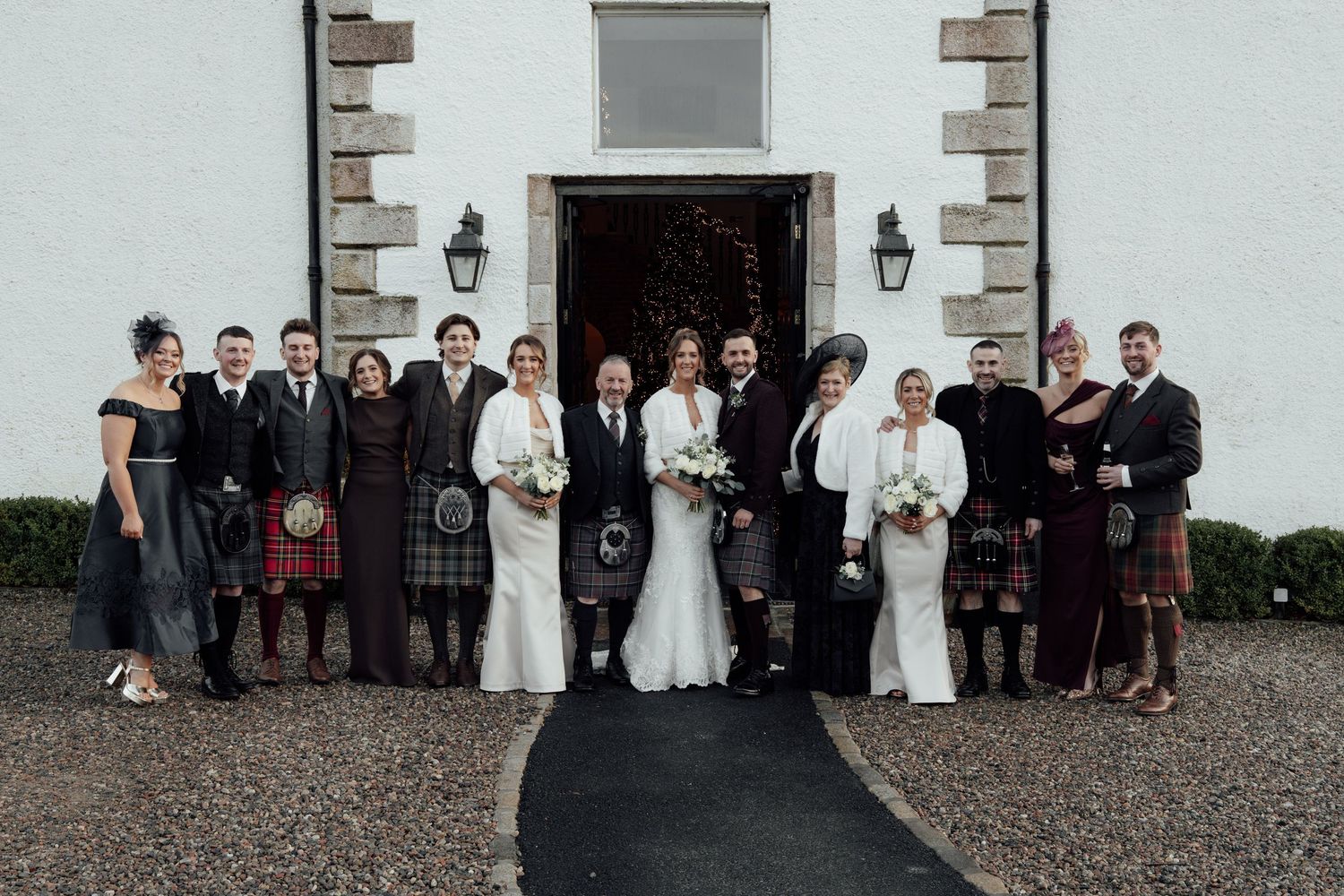 Wedding party members gathered outside a white stone building with traditional lanterns and architectural details.