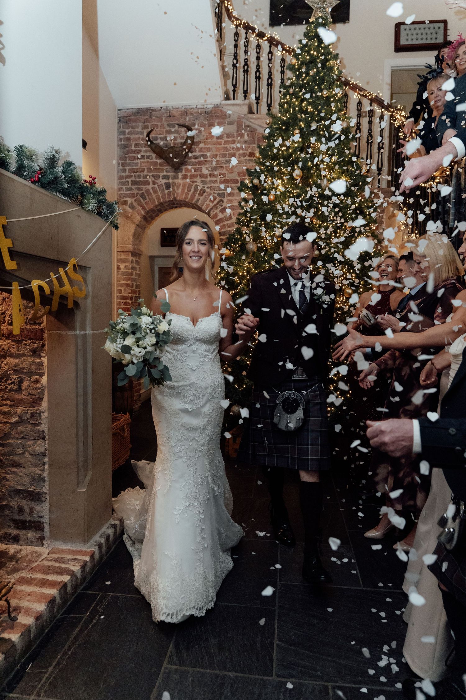 Winter wedding celebration with confetti shower and decorated Christmas tree in brick venue.