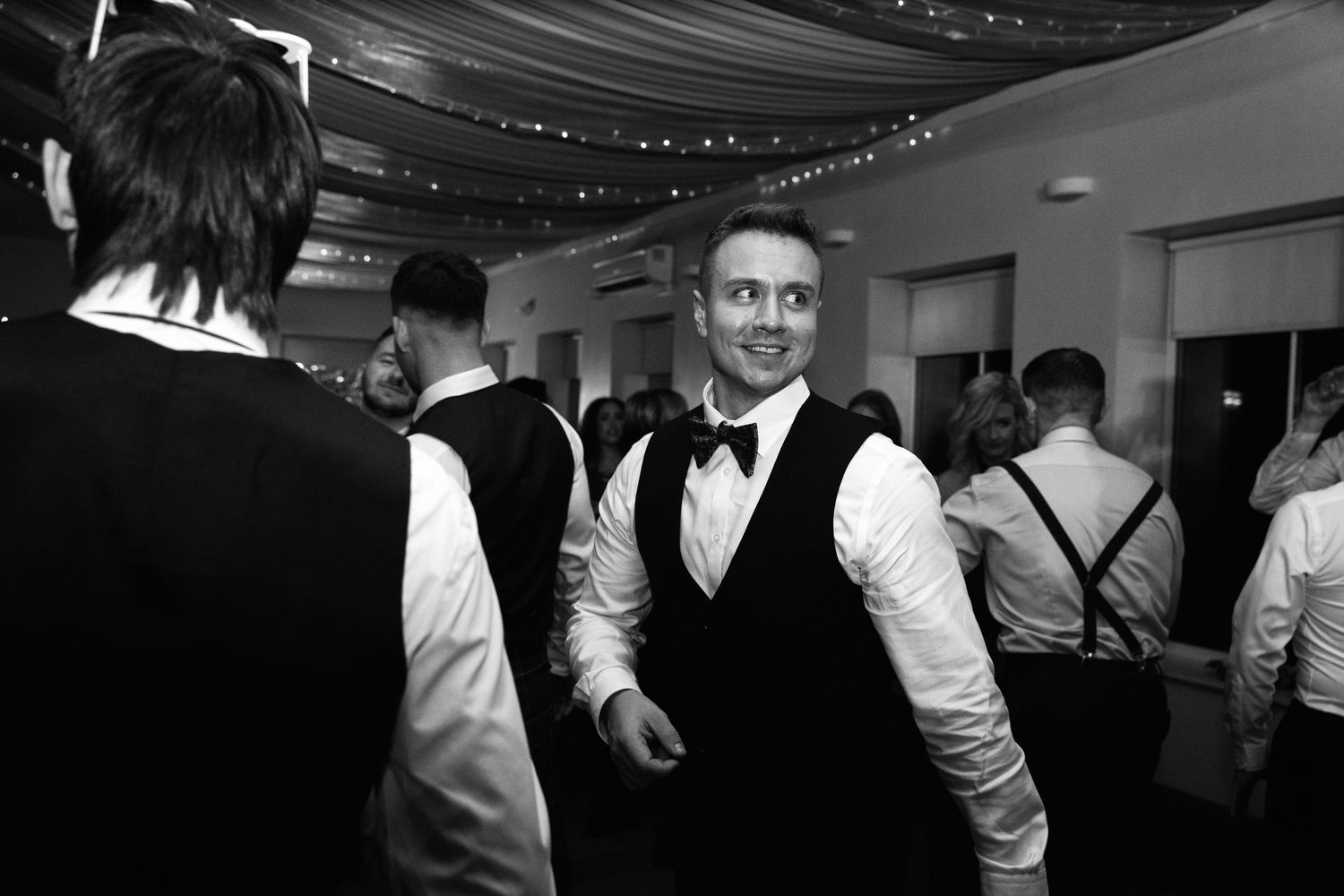 Black and white photo of guests in formal attire mingling at an indoor wedding reception.