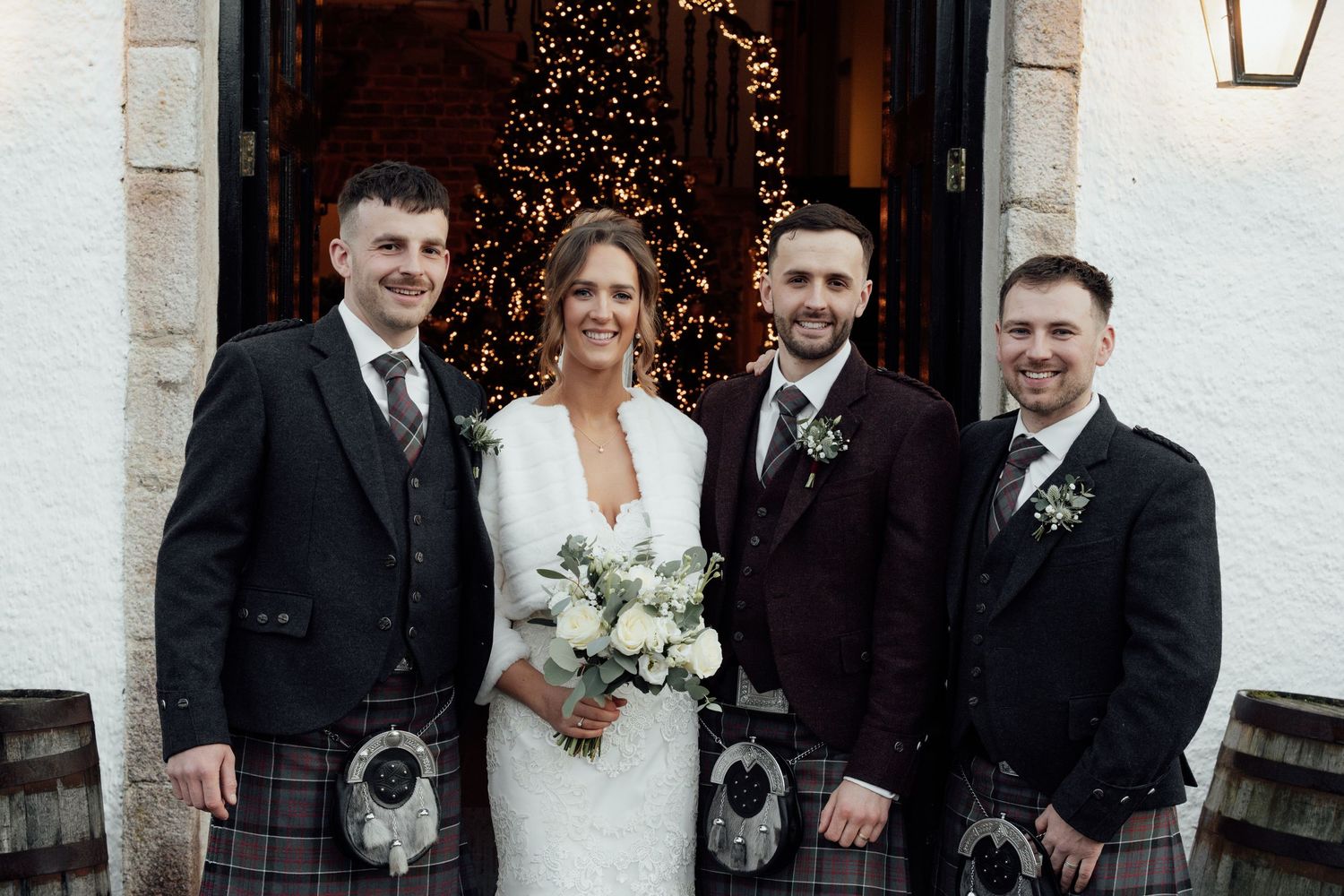 Wedding group in formal attire and Scottish kilts posing outside venue with traditional architecture.