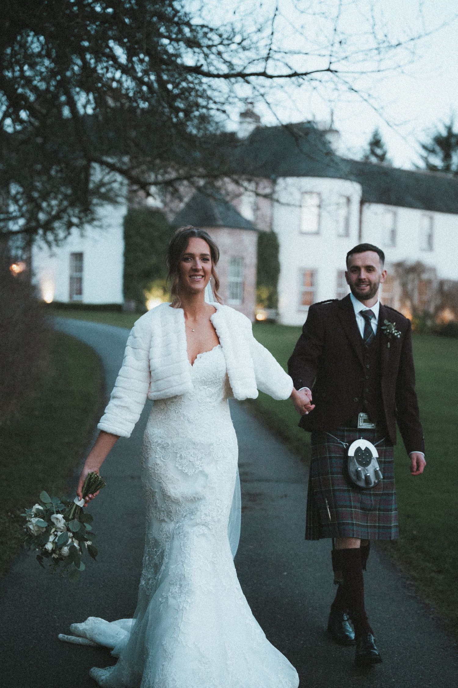 A couple shares a joyful moment while walking along a path outside a historic white building.