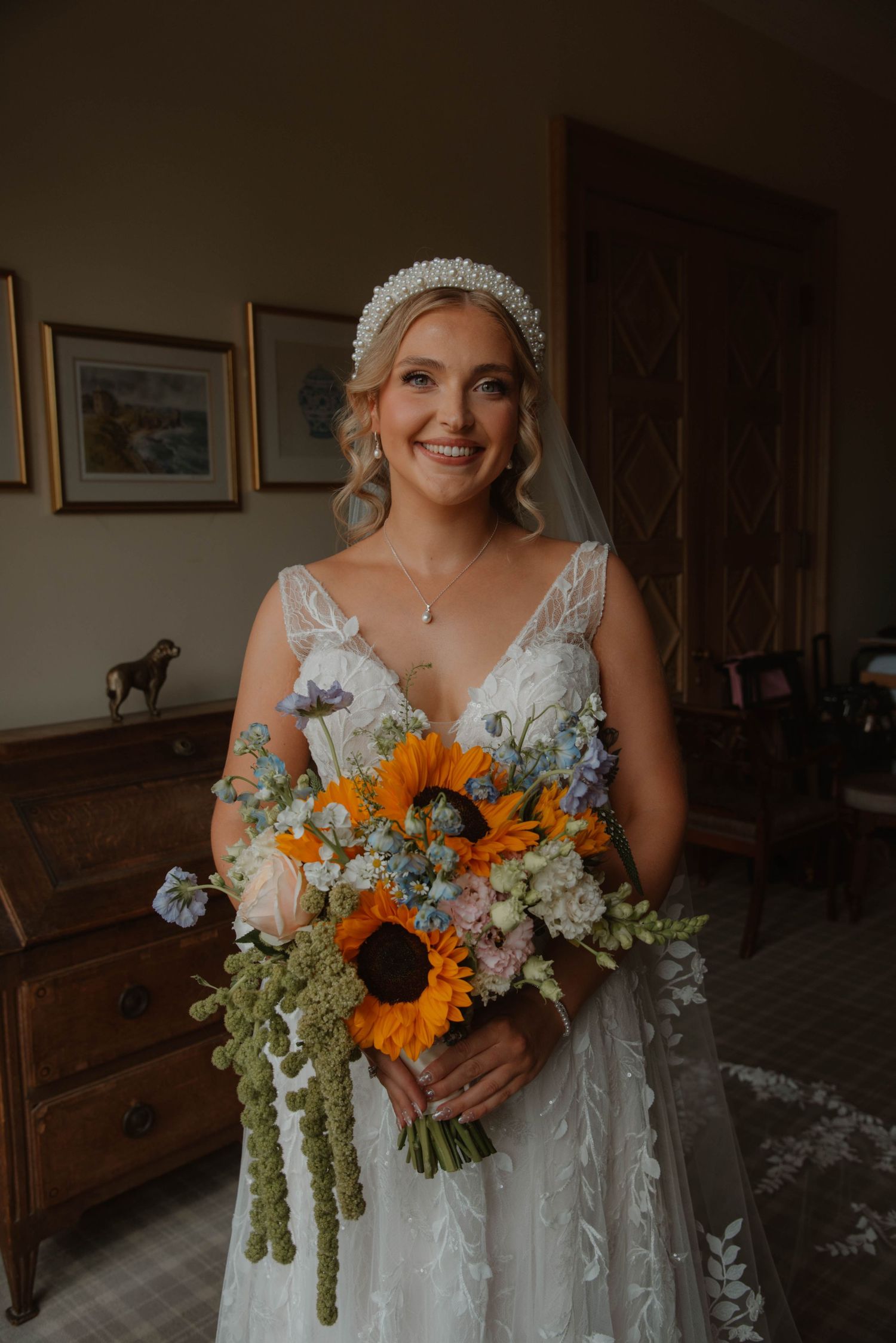 Bride holding vibrant sunflower and wildflower bouquet in a rustic indoor setting.